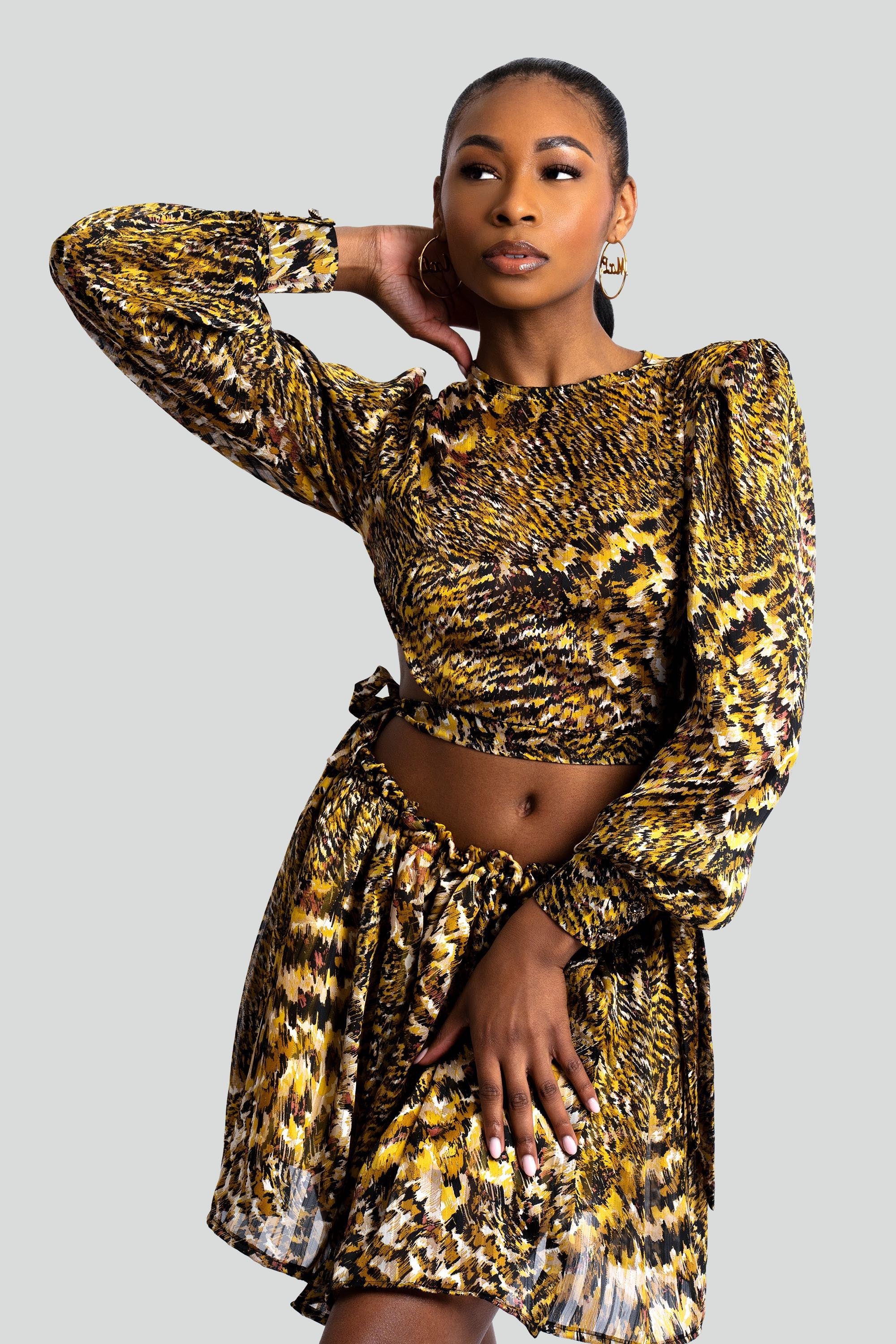 Woman in a gold and black patterned two-piece skirt set posing against a white background