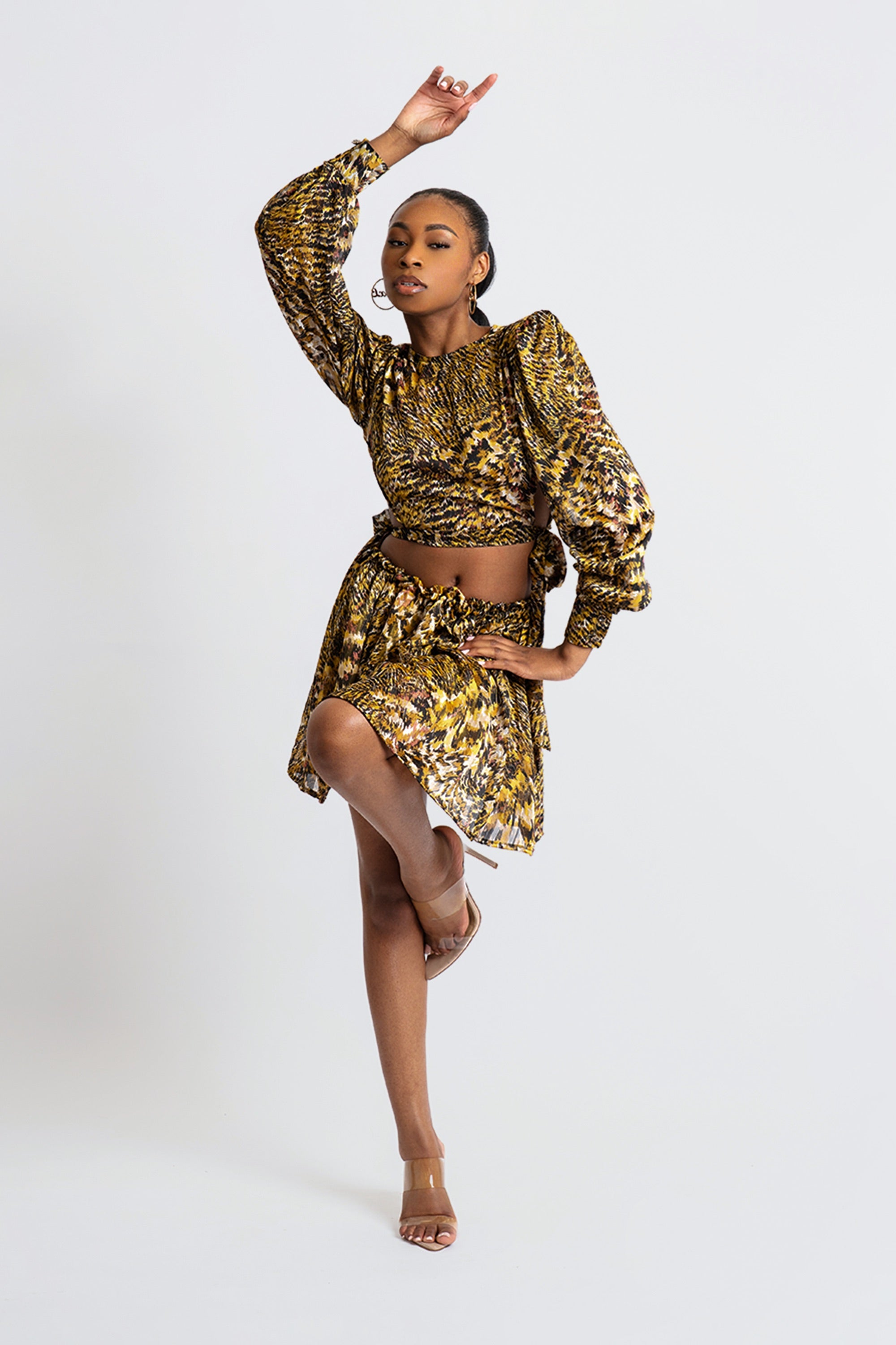 Woman in a gold and black patterned two-piece skirt set posing against a white background
