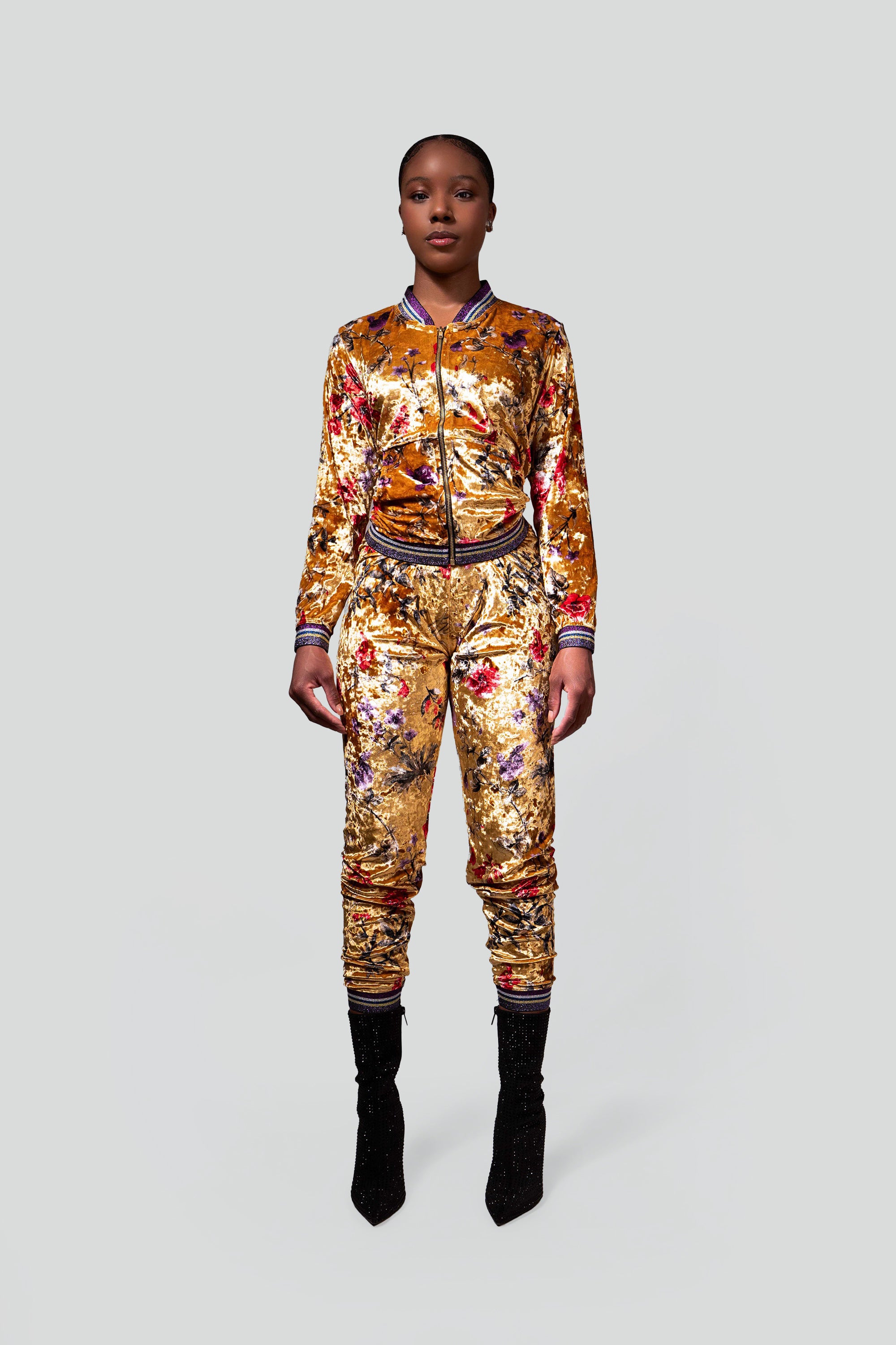 Woman wearing a gold velour tracksuit with red and purple floral accents