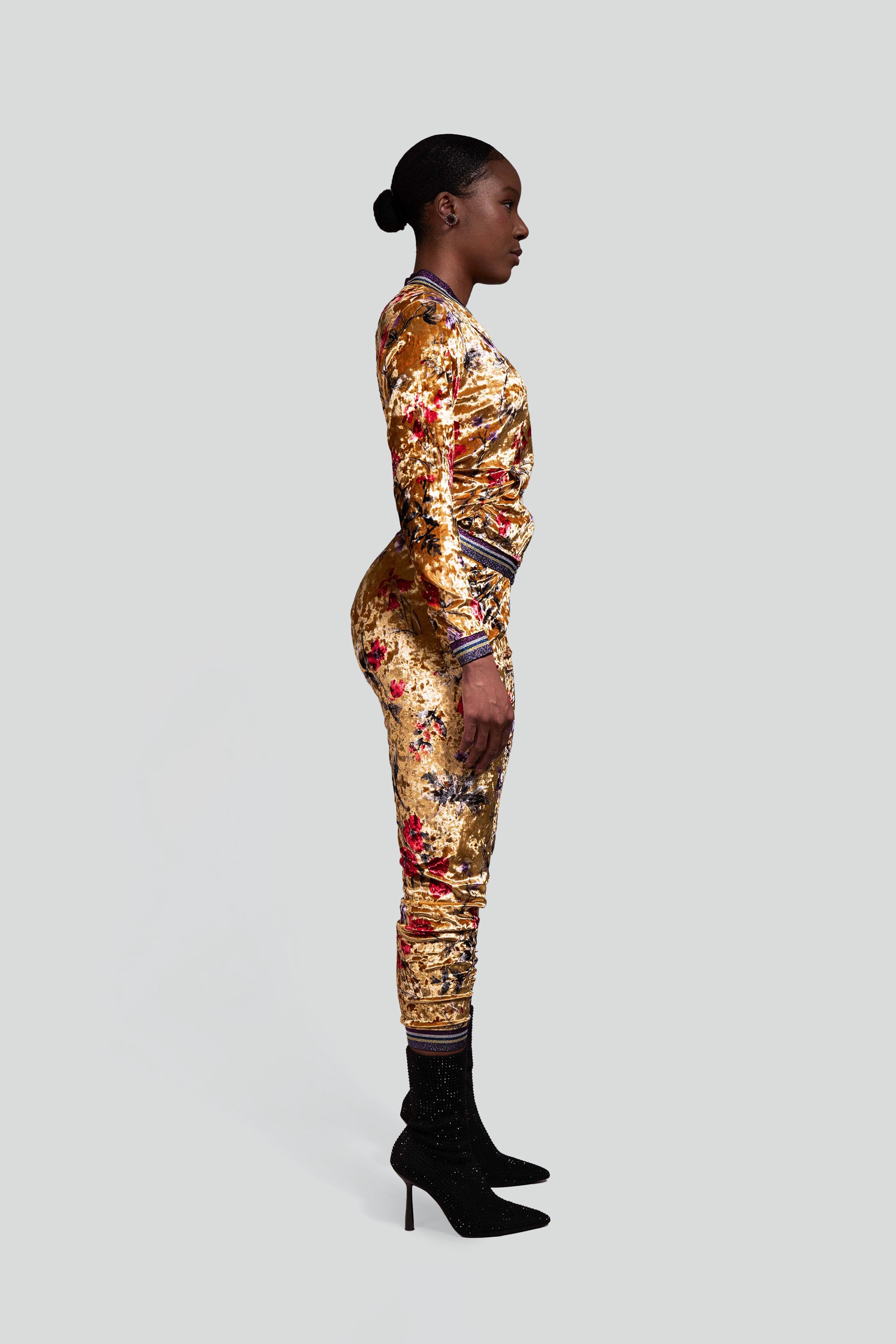 Side view of a woman wearing a gold velour tracksuit with red and purple floral accents