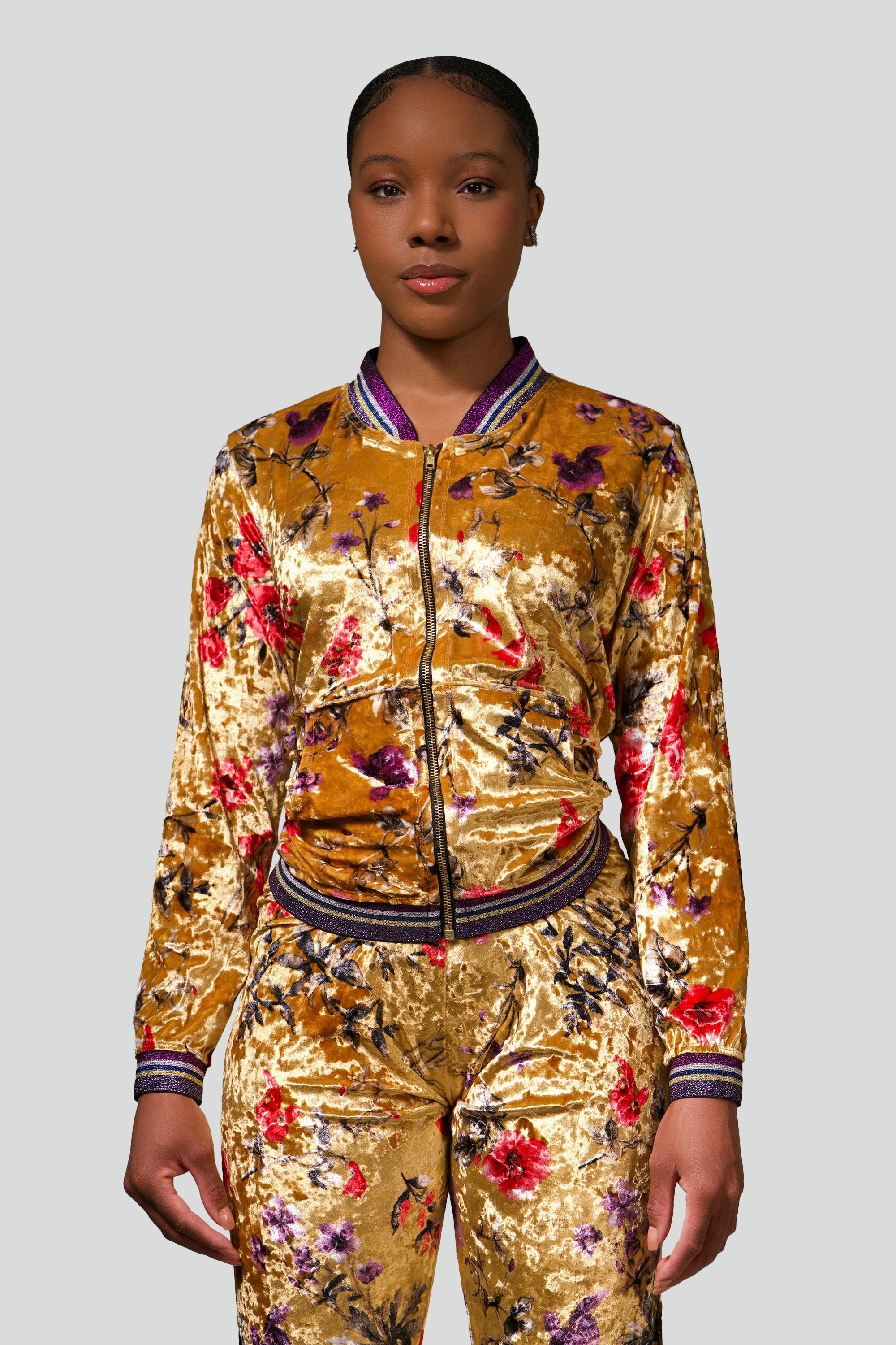 Woman wearing a gold velour tracksuit with red and purple floral accents