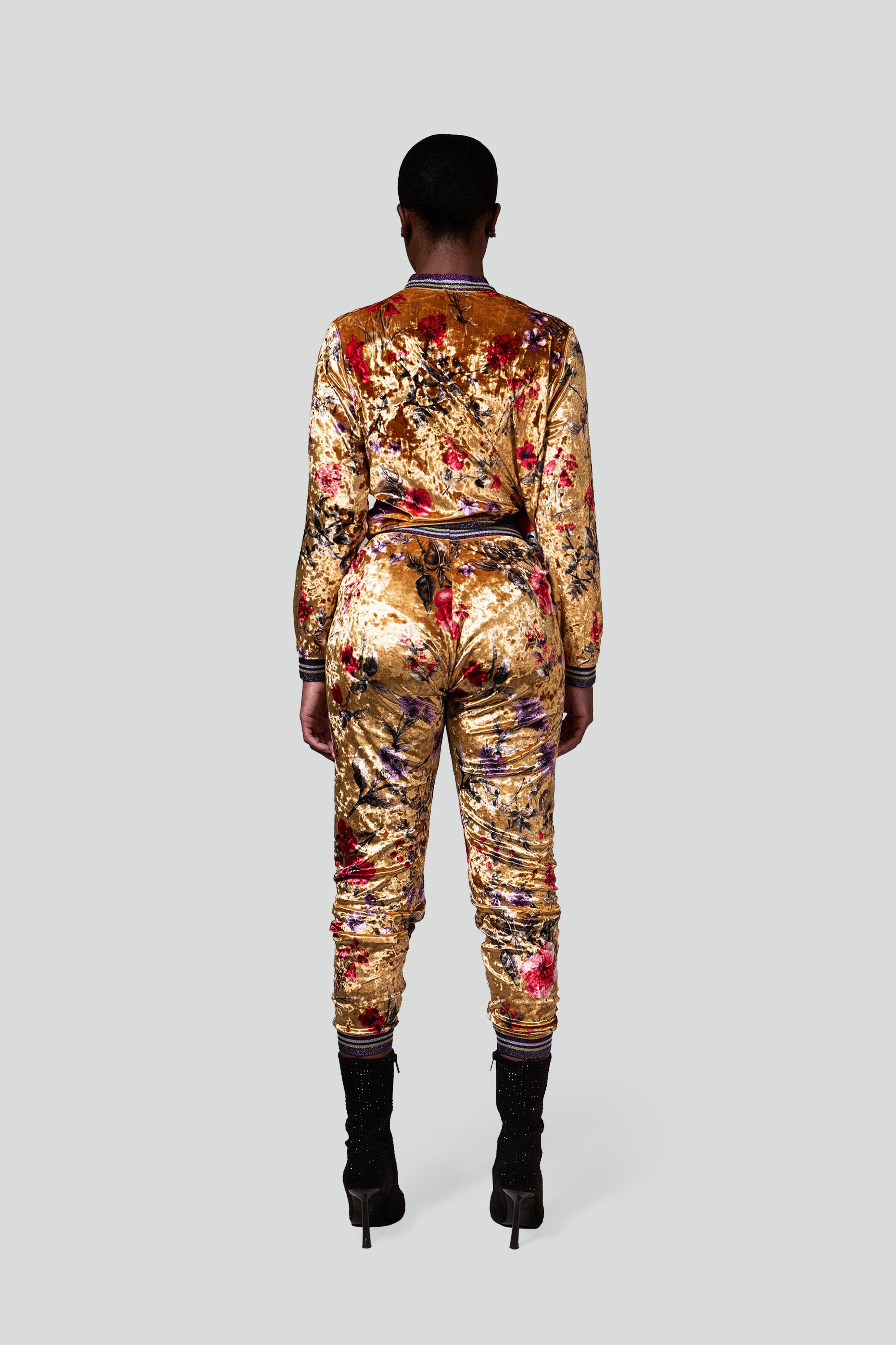 Back view of a woman wearing a gold velour tracksuit with red and purple floral accents
