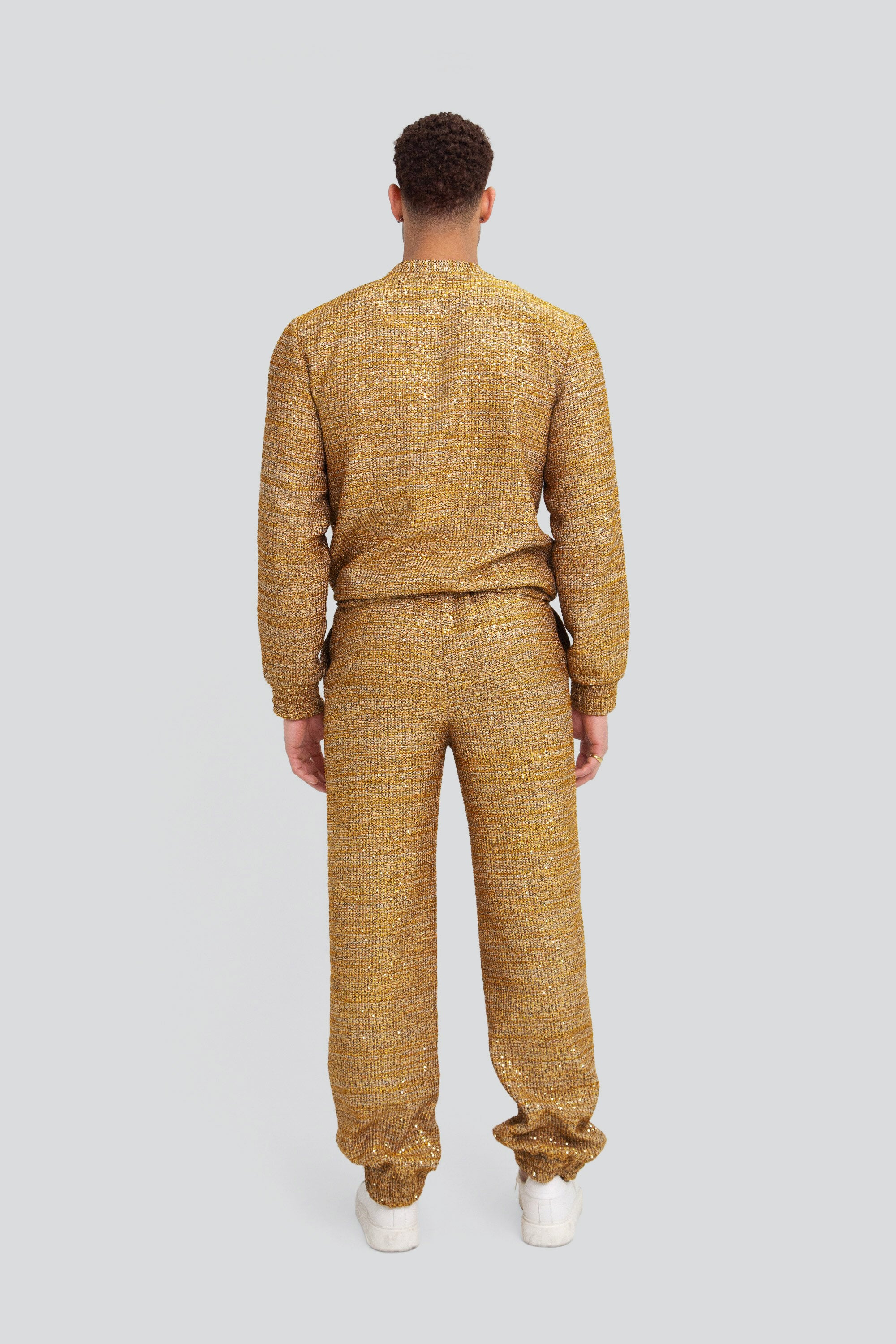 Back view of a man wearing a gold textured sweater and pants on a plain background