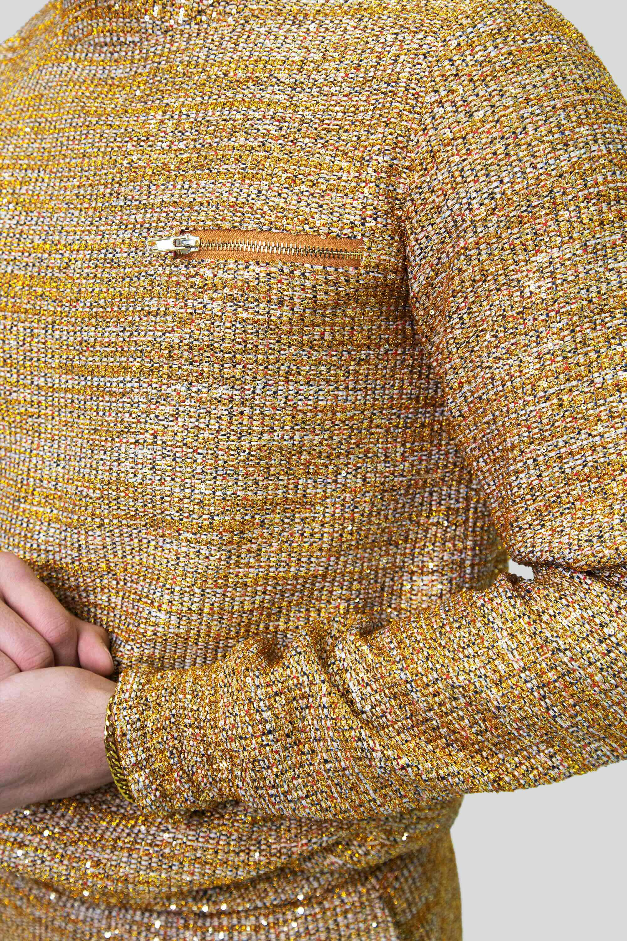 Close-up of a gold textured sweater with a zipper detail on a plain background