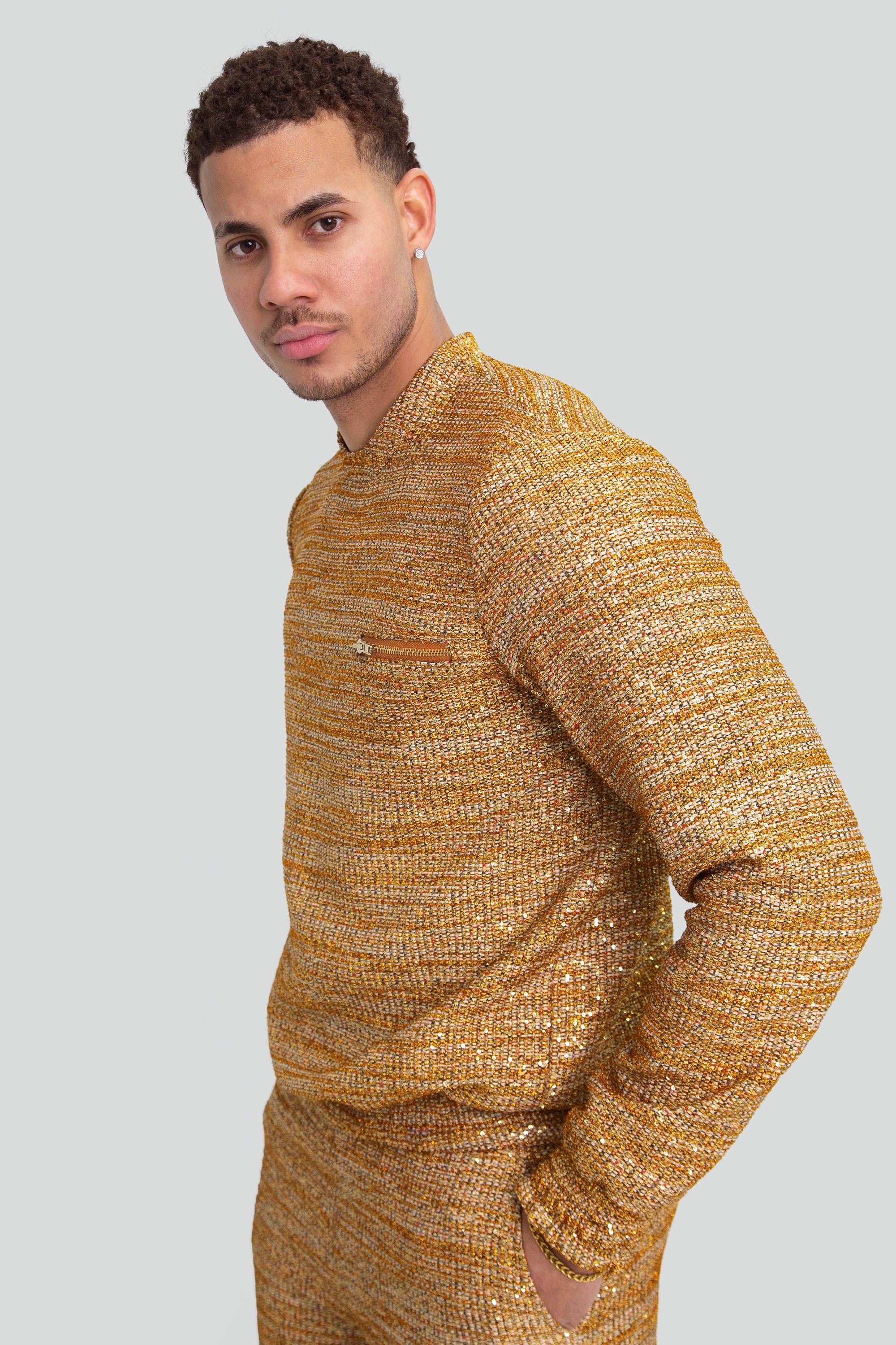 Close up of a man wearing a gold textured sweater on a plain background