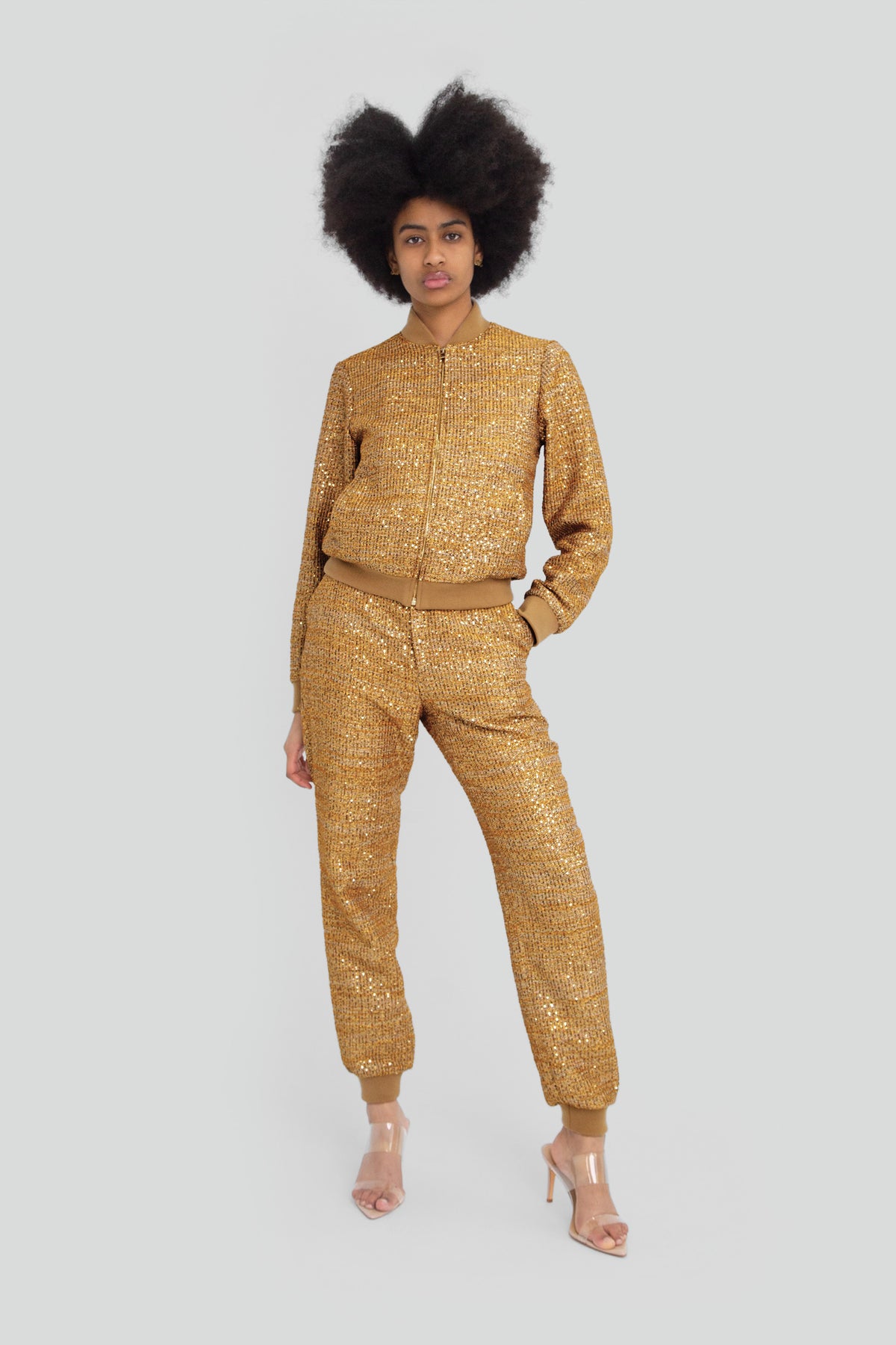 Woman wearing a gold metallic and tweed tracksuit featuring a relaxed zip up track jacket with a structured mock neck and matching straight leg pants