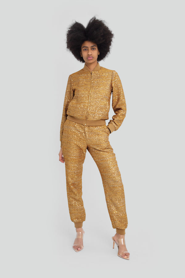 Woman wearing a gold metallic and tweed tracksuit featuring a relaxed zip up track jacket with a structured mock neck and matching straight leg pants