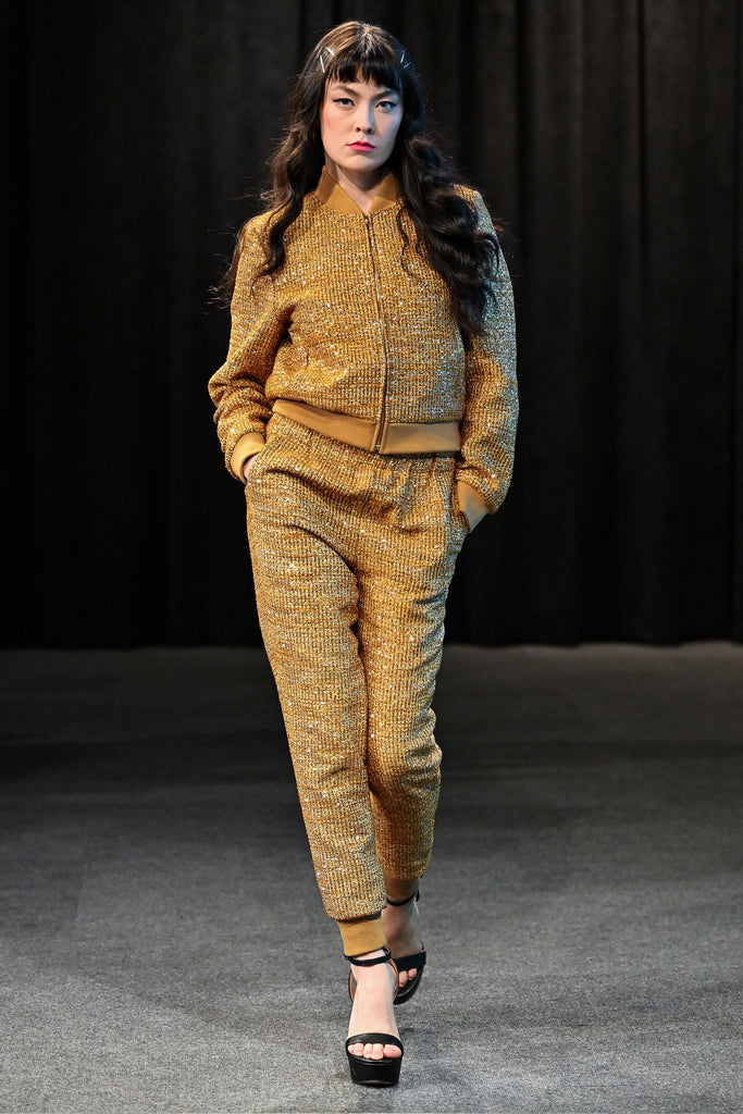 Model wearing a gold textured tracksuit on a dark background