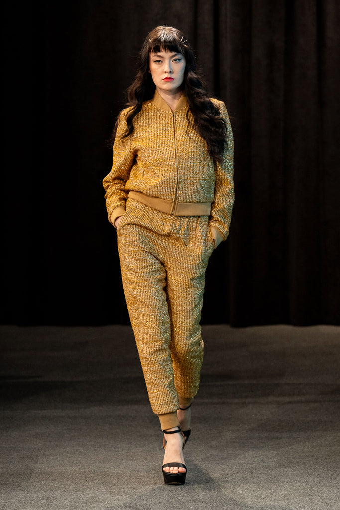 Model wearing a gold textured tracksuit on a dark background