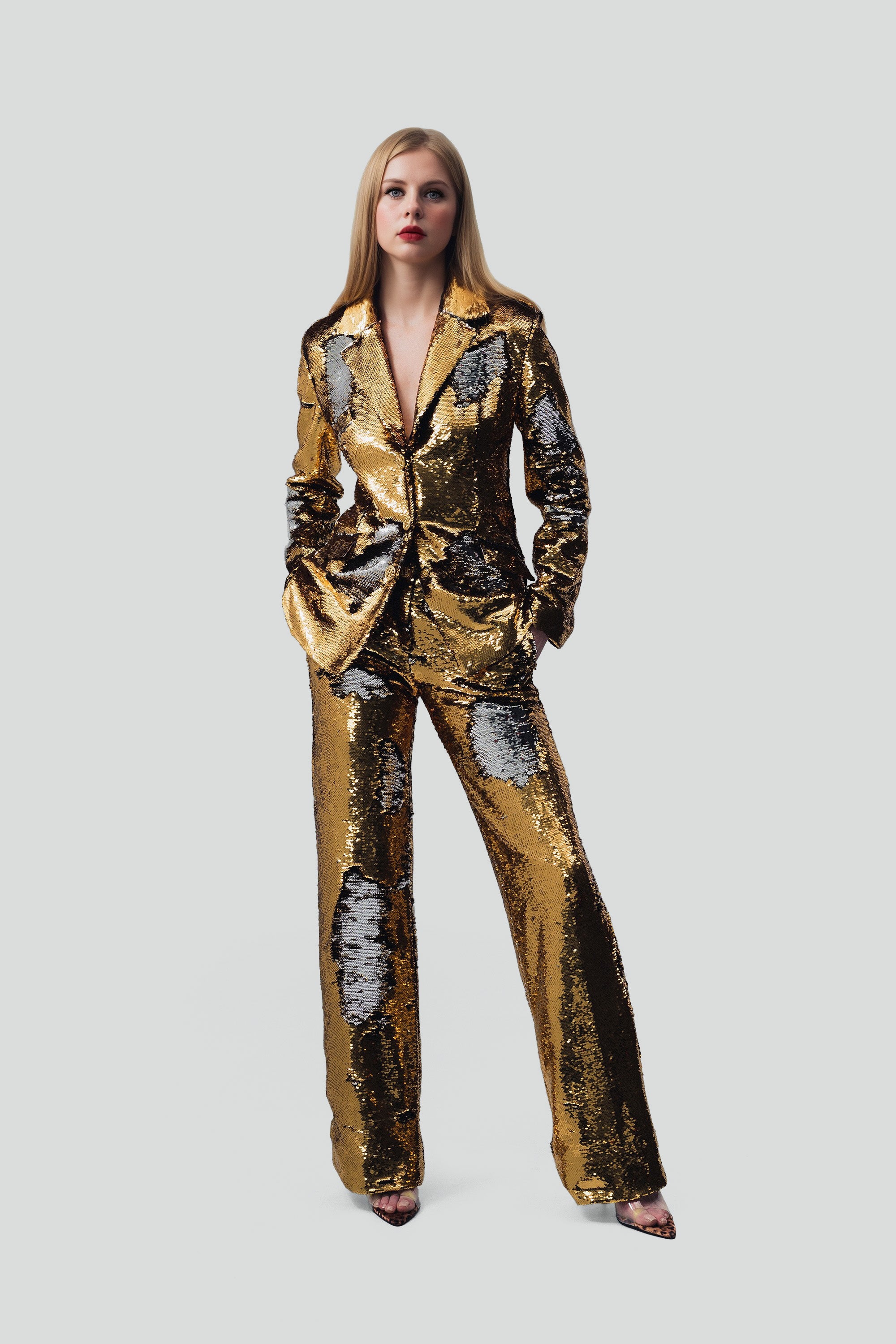 Woman wearing gold sequin blazer and pants set on a grey background