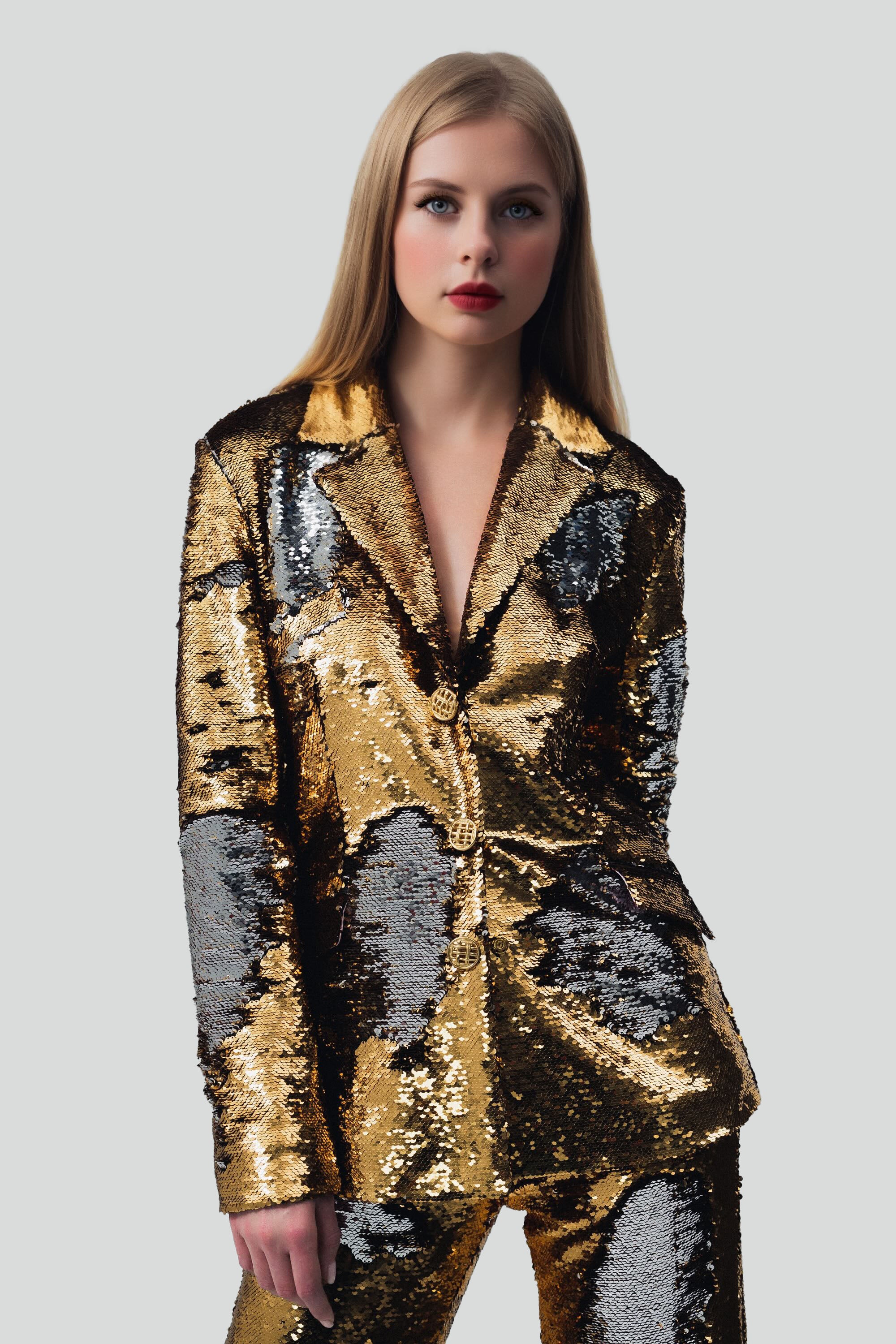 Woman wearing gold sequin blazer and pants set with a grey background