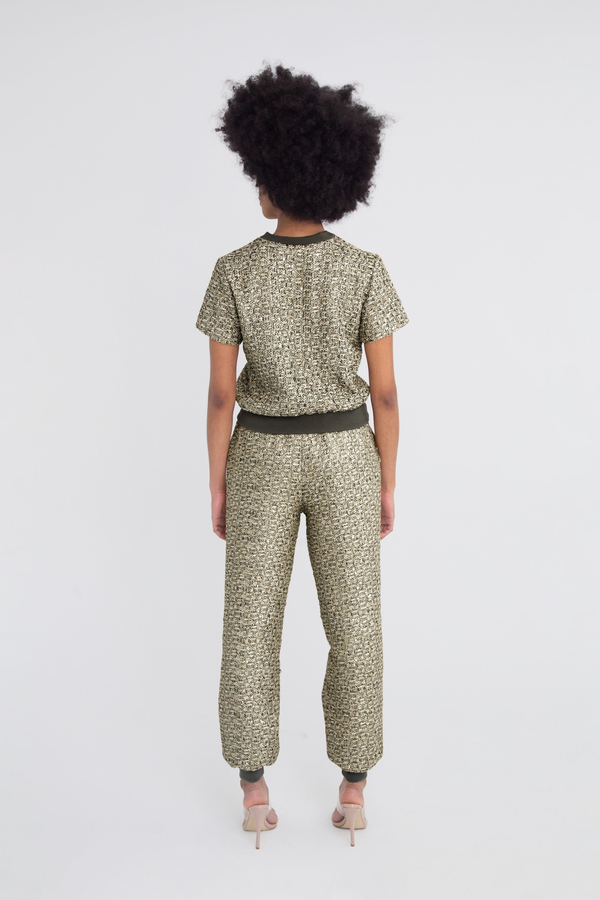 Woman wearing a green metallic textured outfit with short sleeves and pants on a plain background