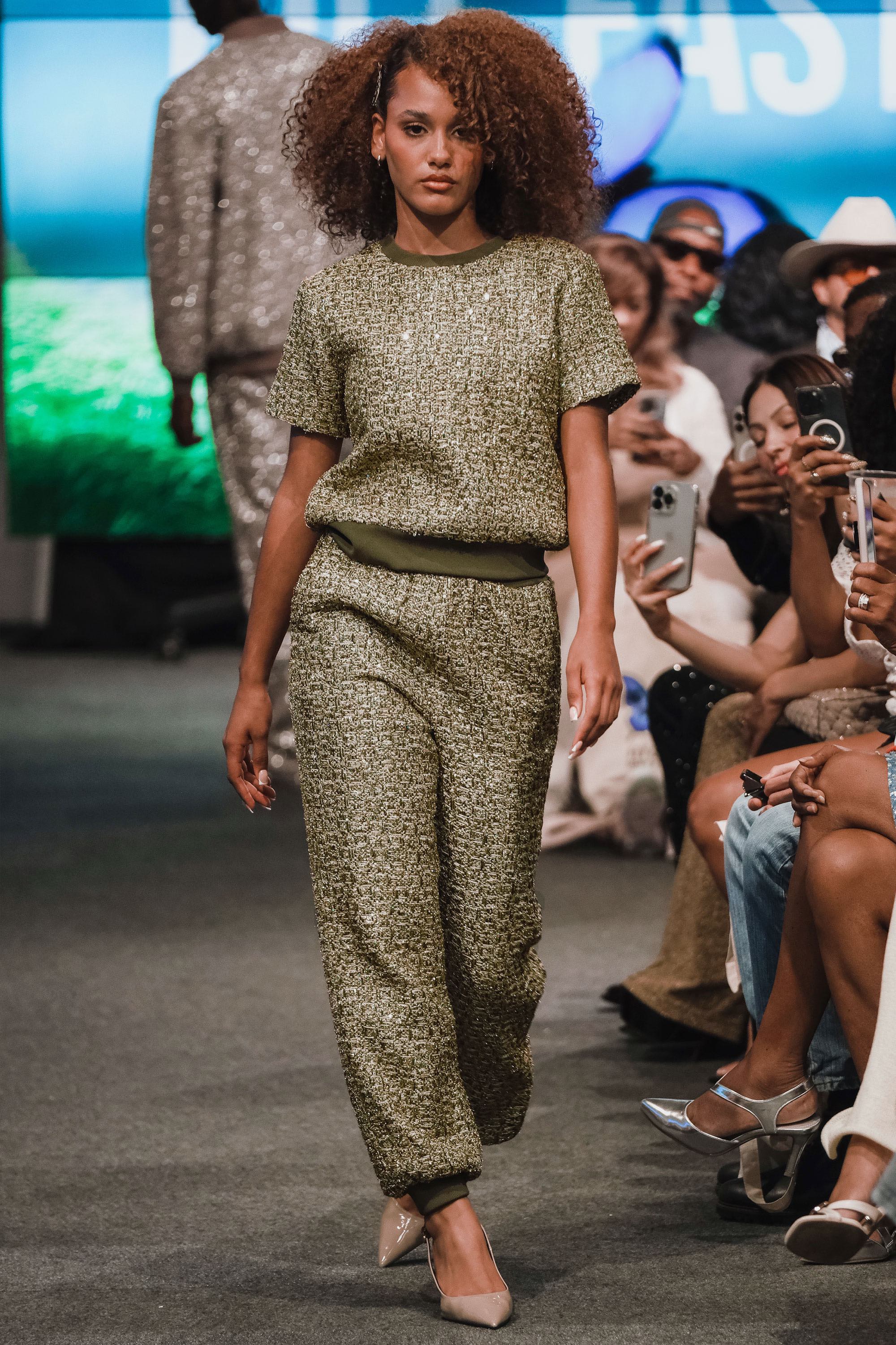 Model walking on a fashion runway wearing a green patterned outfit.