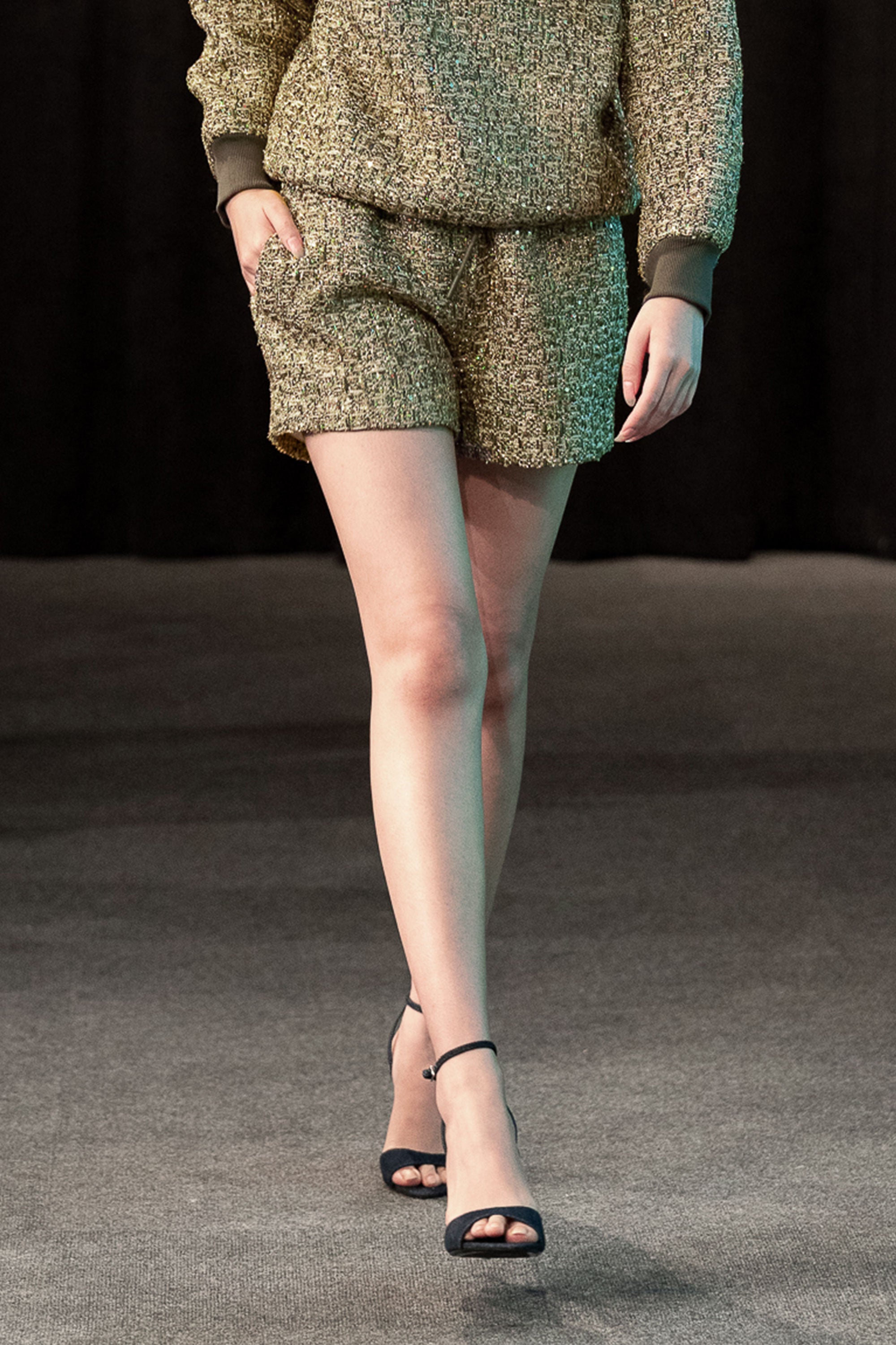 Person wearing a green textured outfit with shorts and a top, walking on a neutral background.