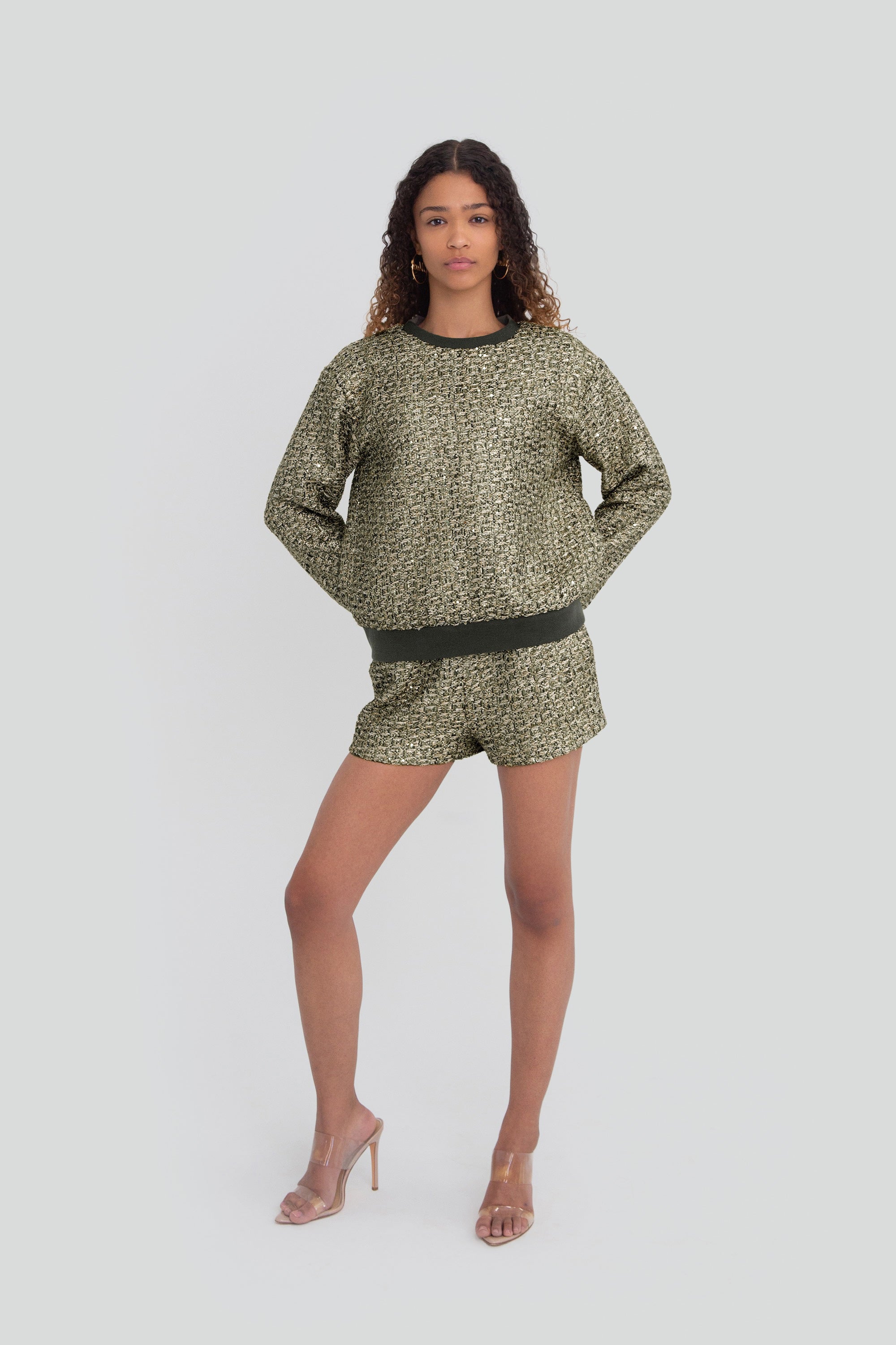 Woman wearing a green metallic textured outfit with shorts and long sleeves on a plain background
