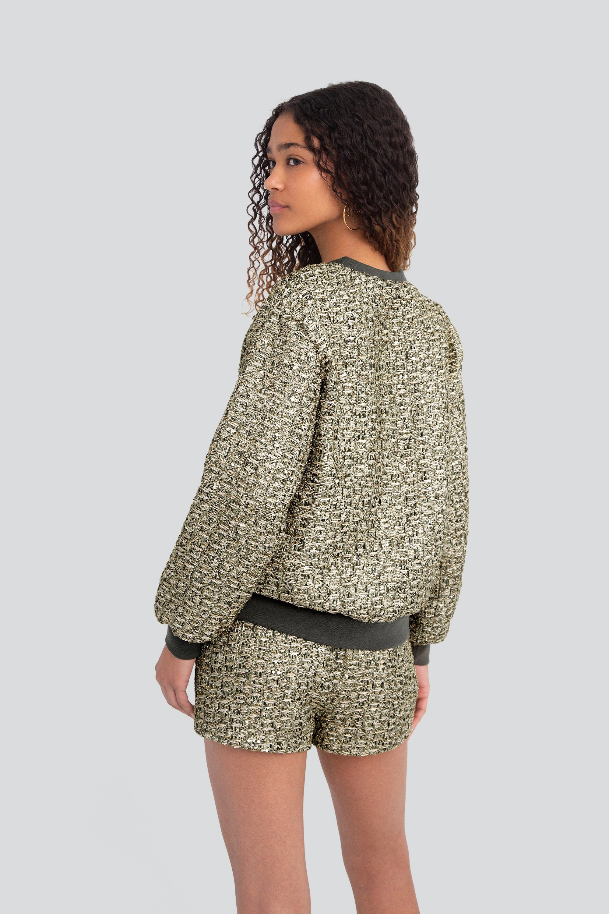 Woman wearing a green metallic textured outfit with long sleeves and shorts on a plain background