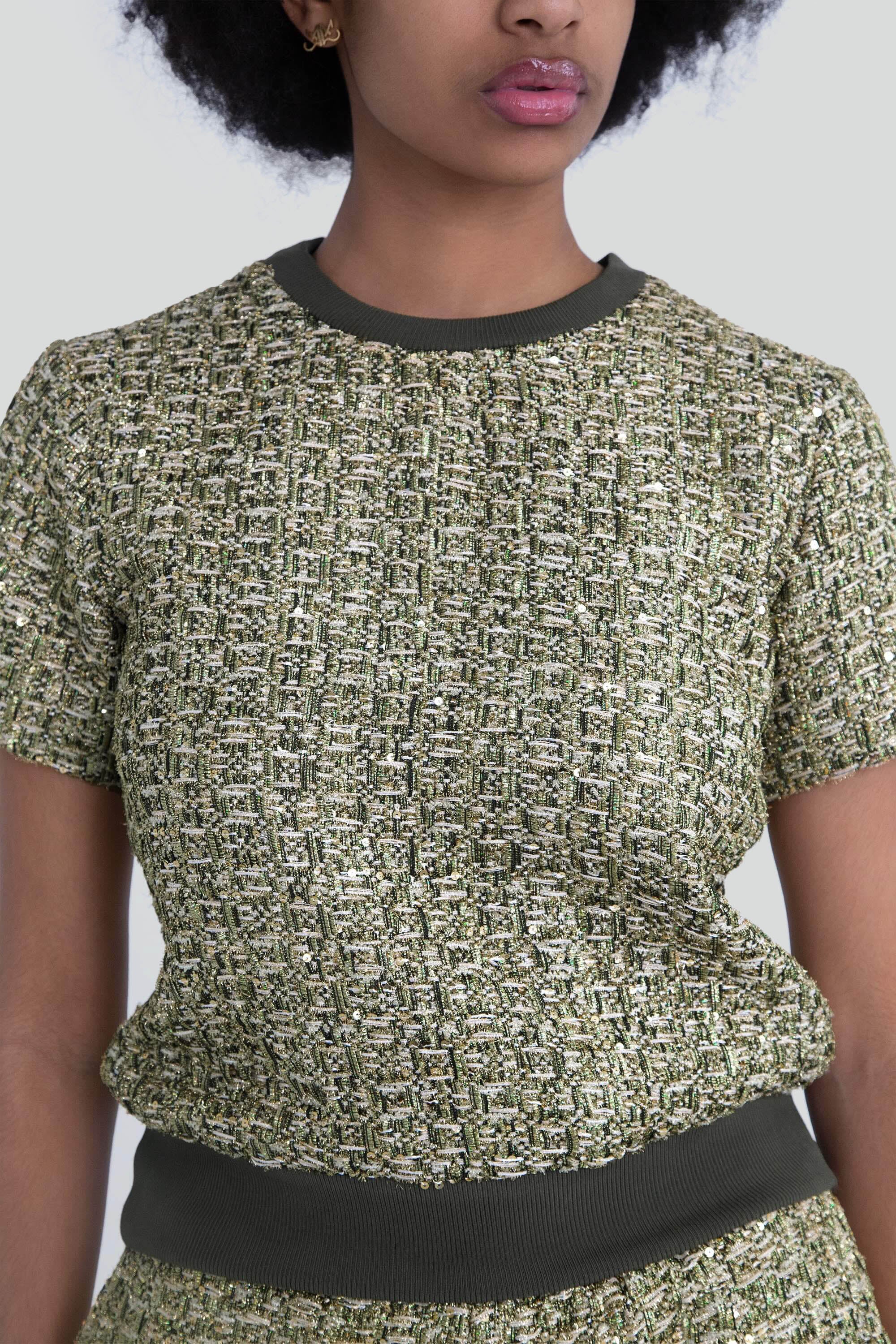 Close up of a woman wearing a green metallic textured top with short sleeves on a plain background