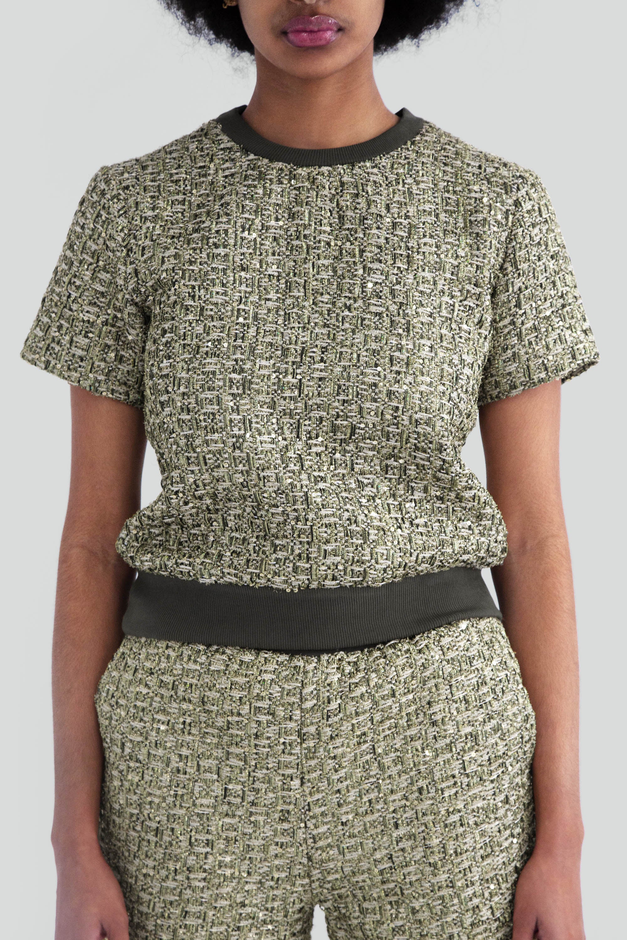 Close up of a woman wearing a green metallic textured top with short sleeves on a plain background