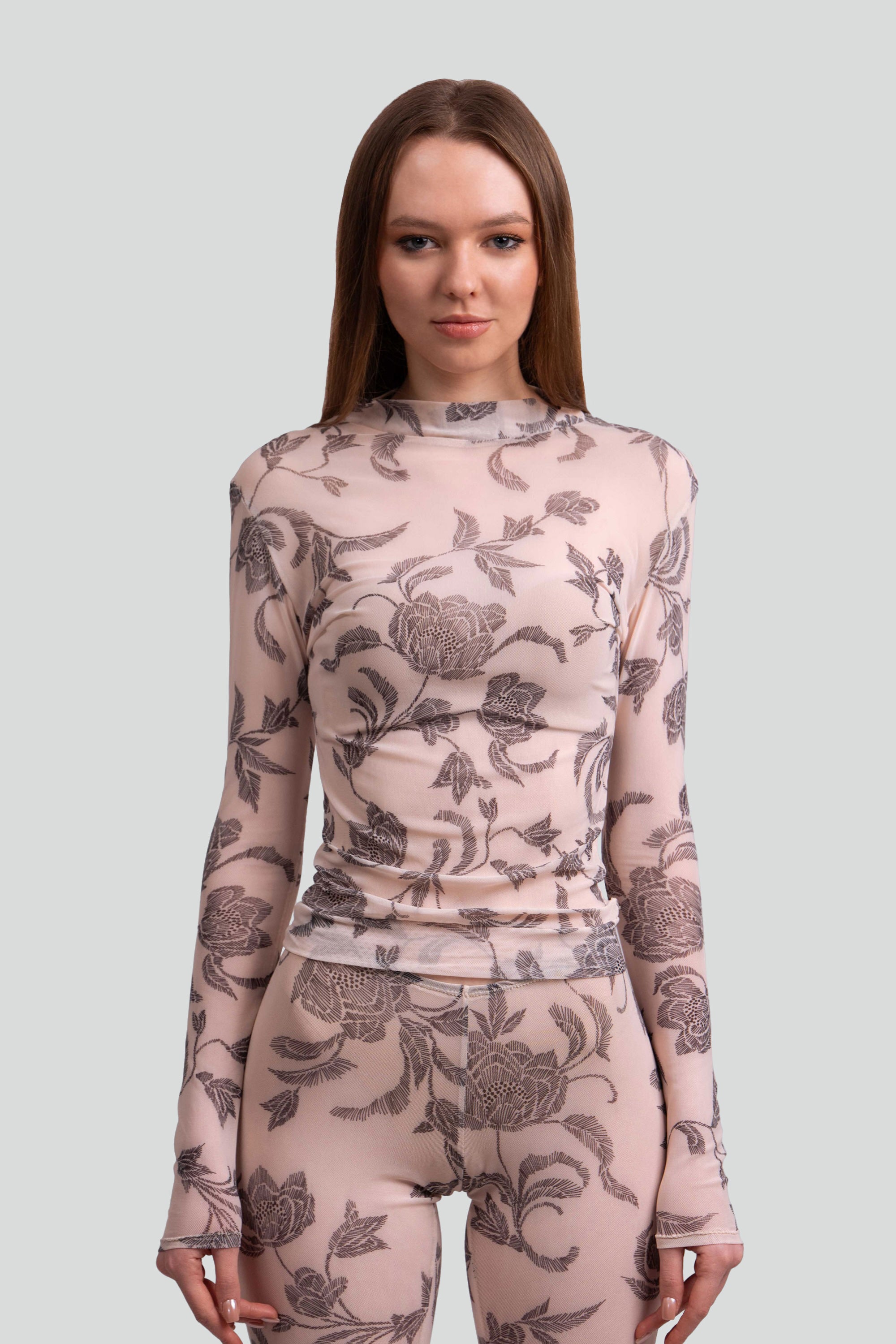 Close up view of a woman wearing a sheer pink and grey floral patterned top and leggings on a plain background