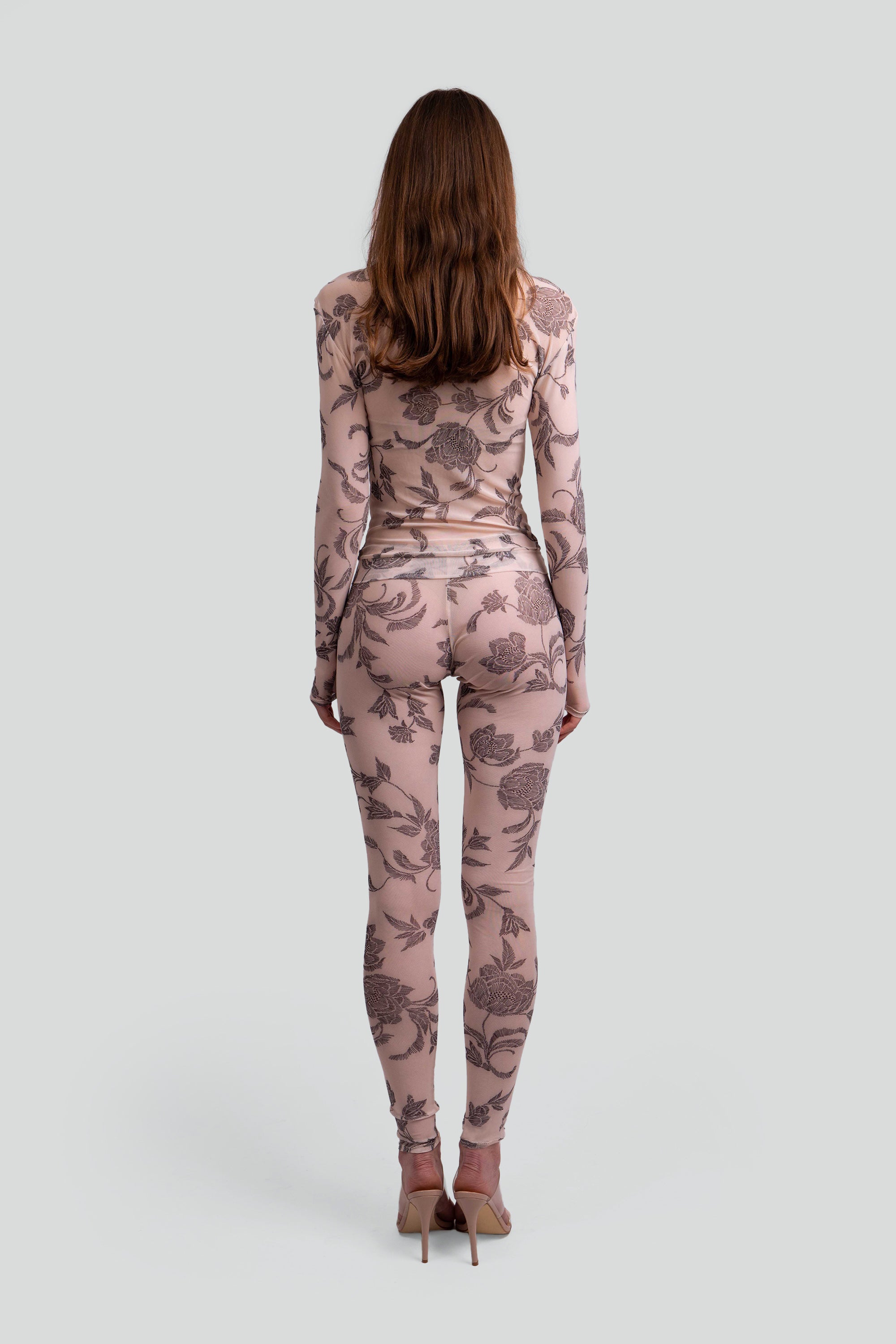 Back view of a woman wearing a sheer pink and grey floral patterned top and leggings on a plain background