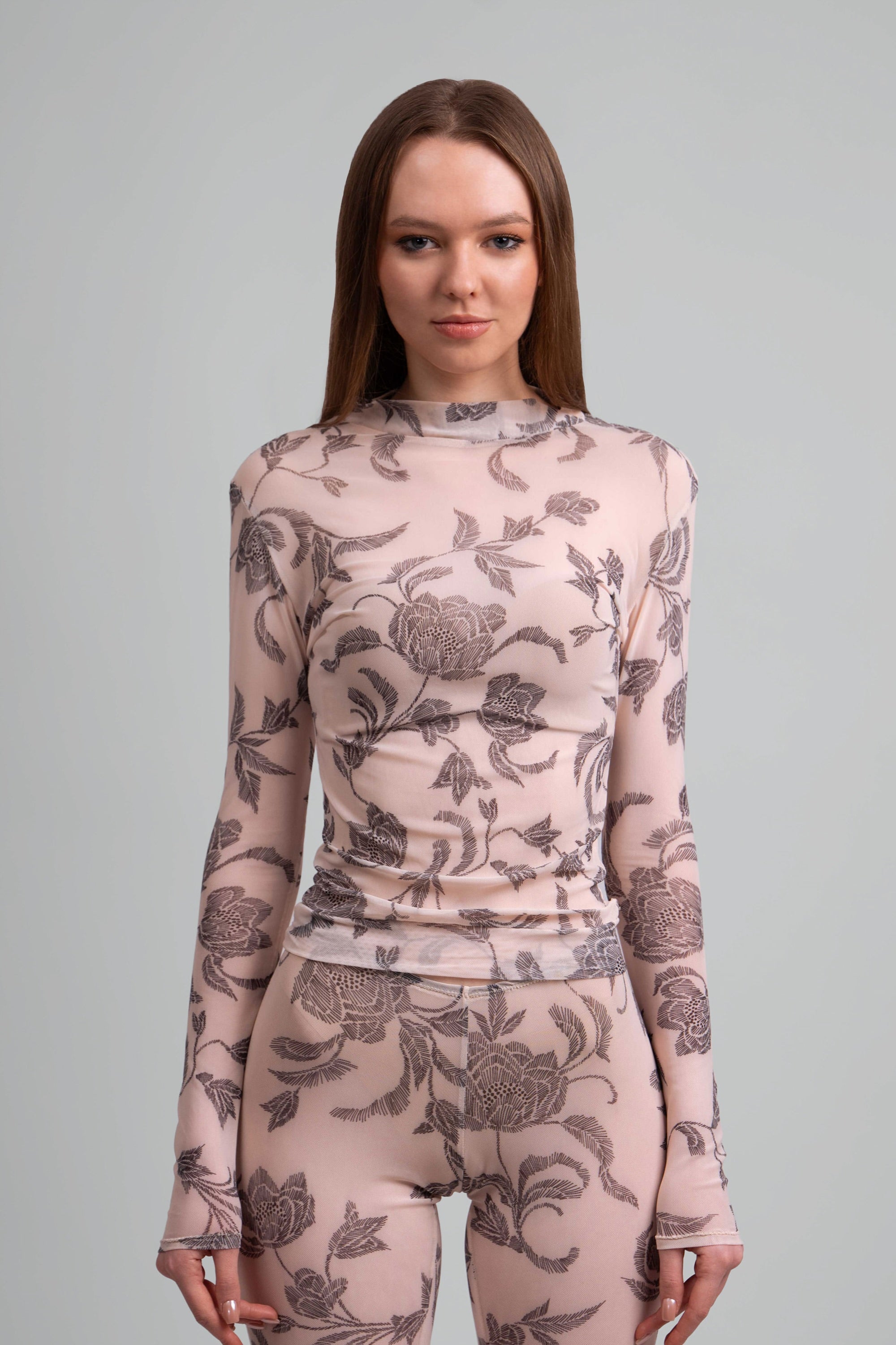 Close up view of a woman wearing a sheer pink and grey floral patterned top and leggings on a plain background