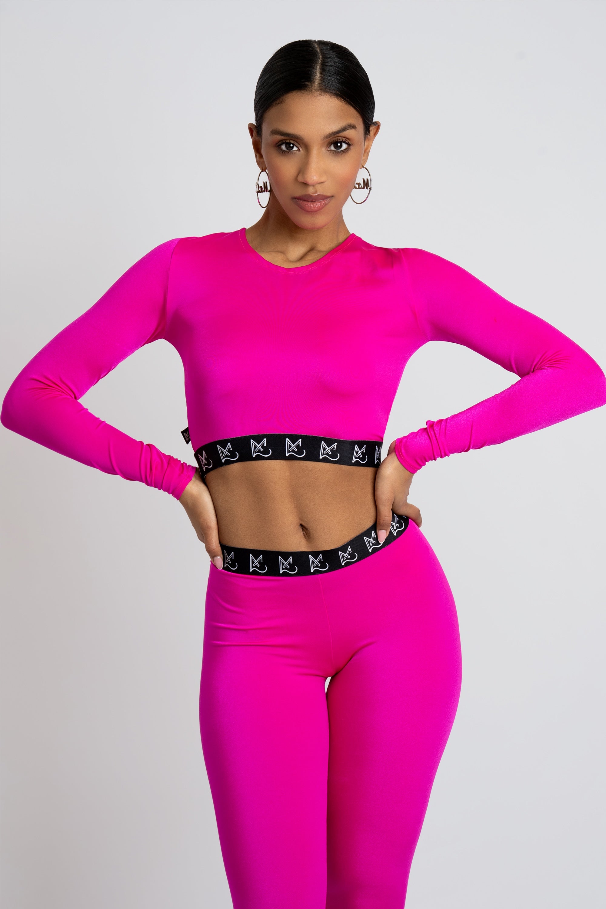 Woman wearing a bright pink long-sleeve crop top and leggings with a black waistband on a light gray background