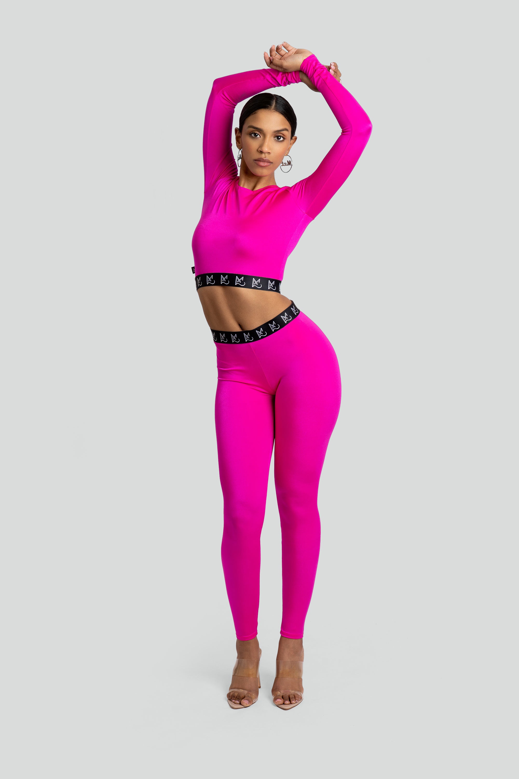 Woman wearing a bright pink long-sleeve crop top and leggings with a black waistband on a light gray background