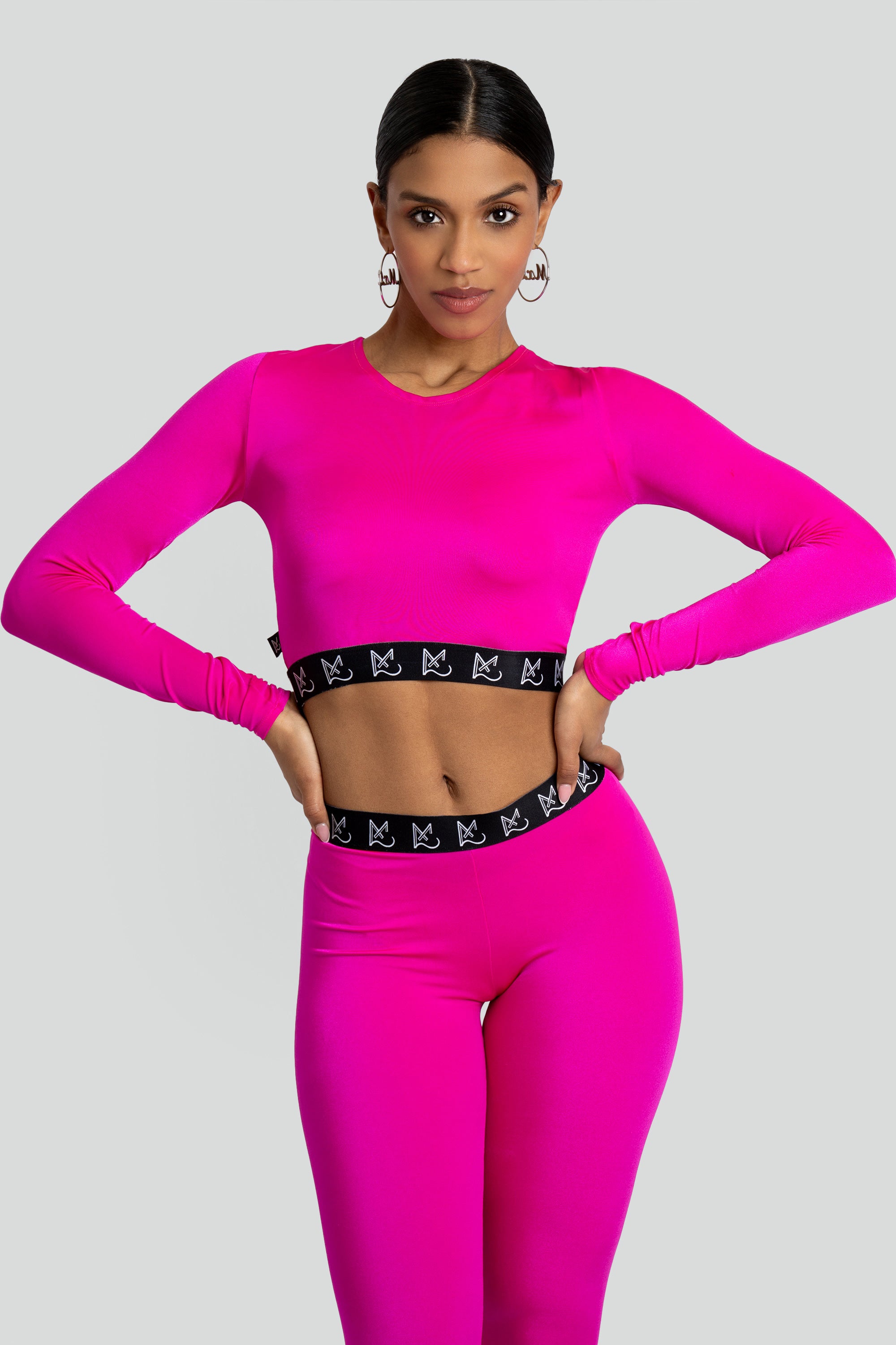 Woman wearing a bright pink long-sleeve crop top and leggings with a black waistband on a light gray background