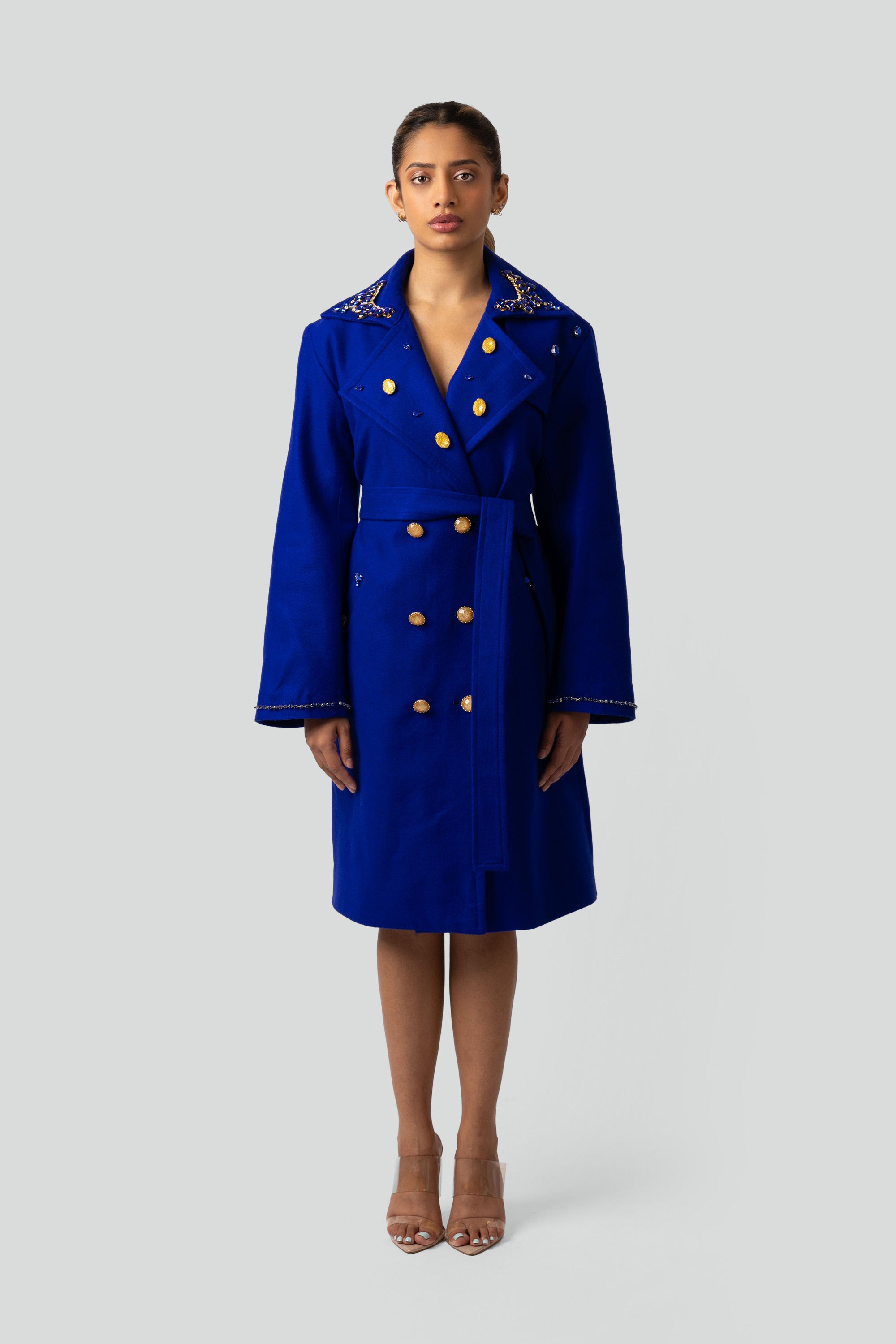 Woman wearing a blue trench coat with gold buttons and gold detailing on a white background