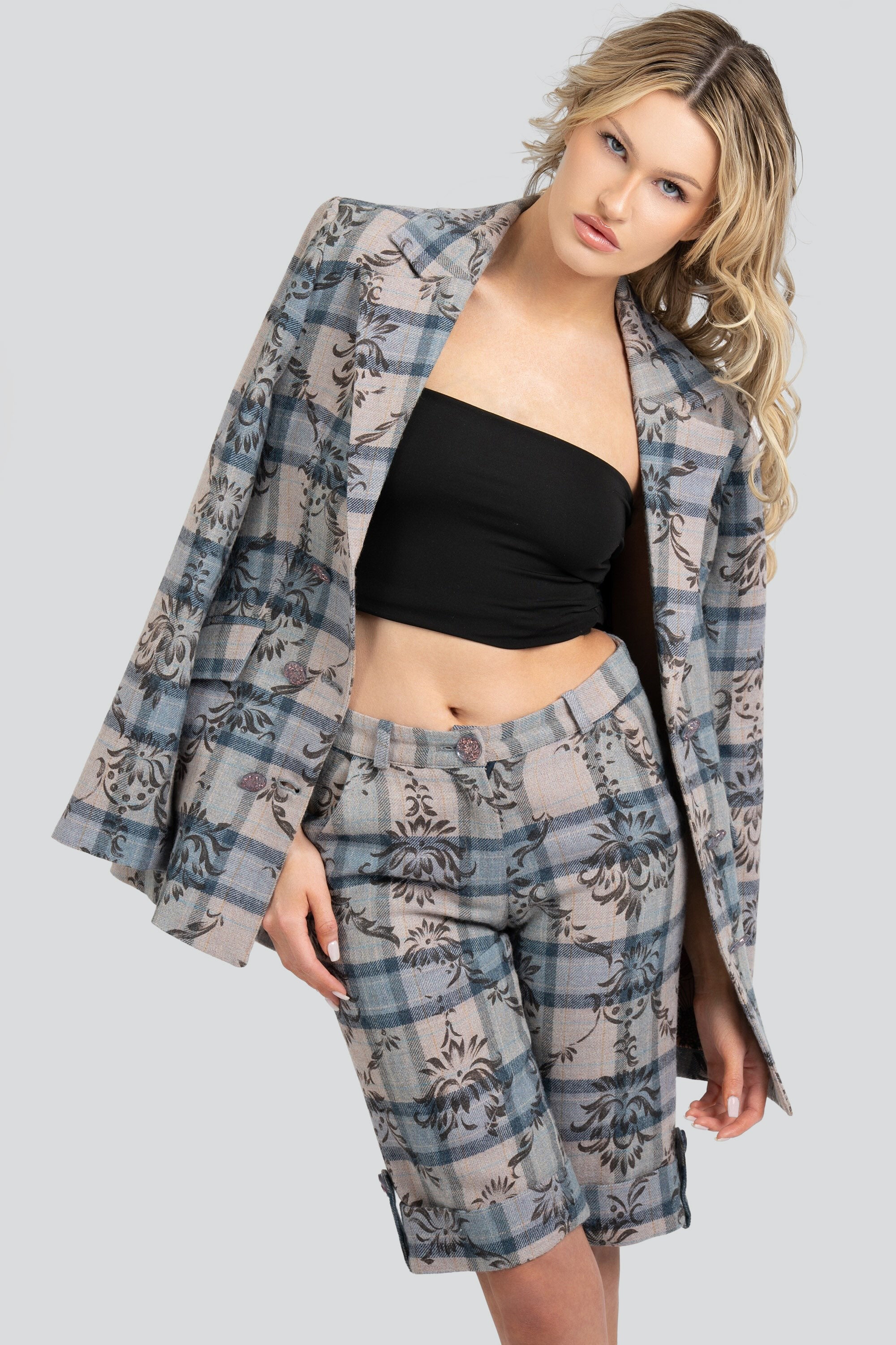 Woman wearing a floral and plaid patterned blazer over her shoulders and matching shorts on a white background