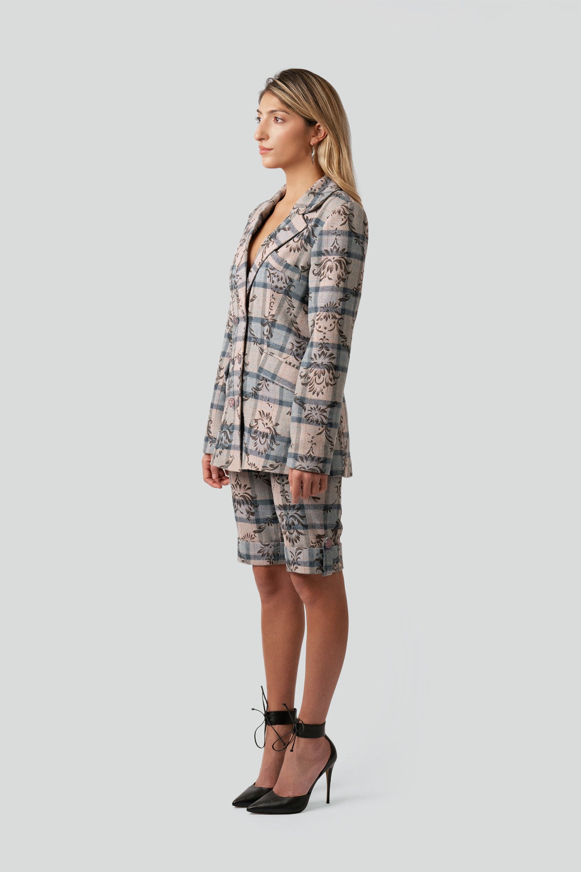 Quarter side view of a woman wearing a floral and plaid patterned blazer and matching shorts on a white background