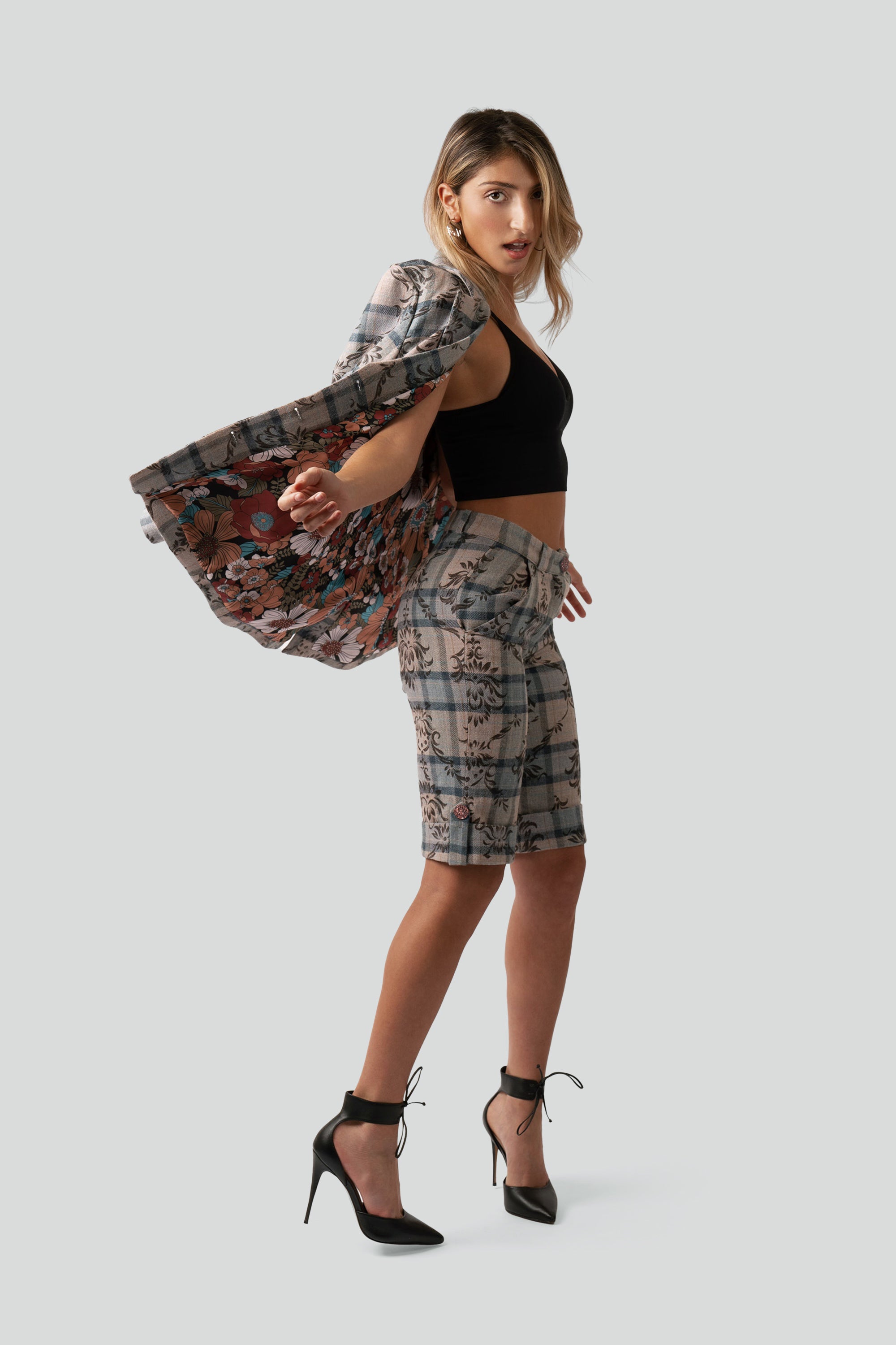 Woman wearing a floral and plaid patterned blazer over her shoulder and matching shorts posing against a white background