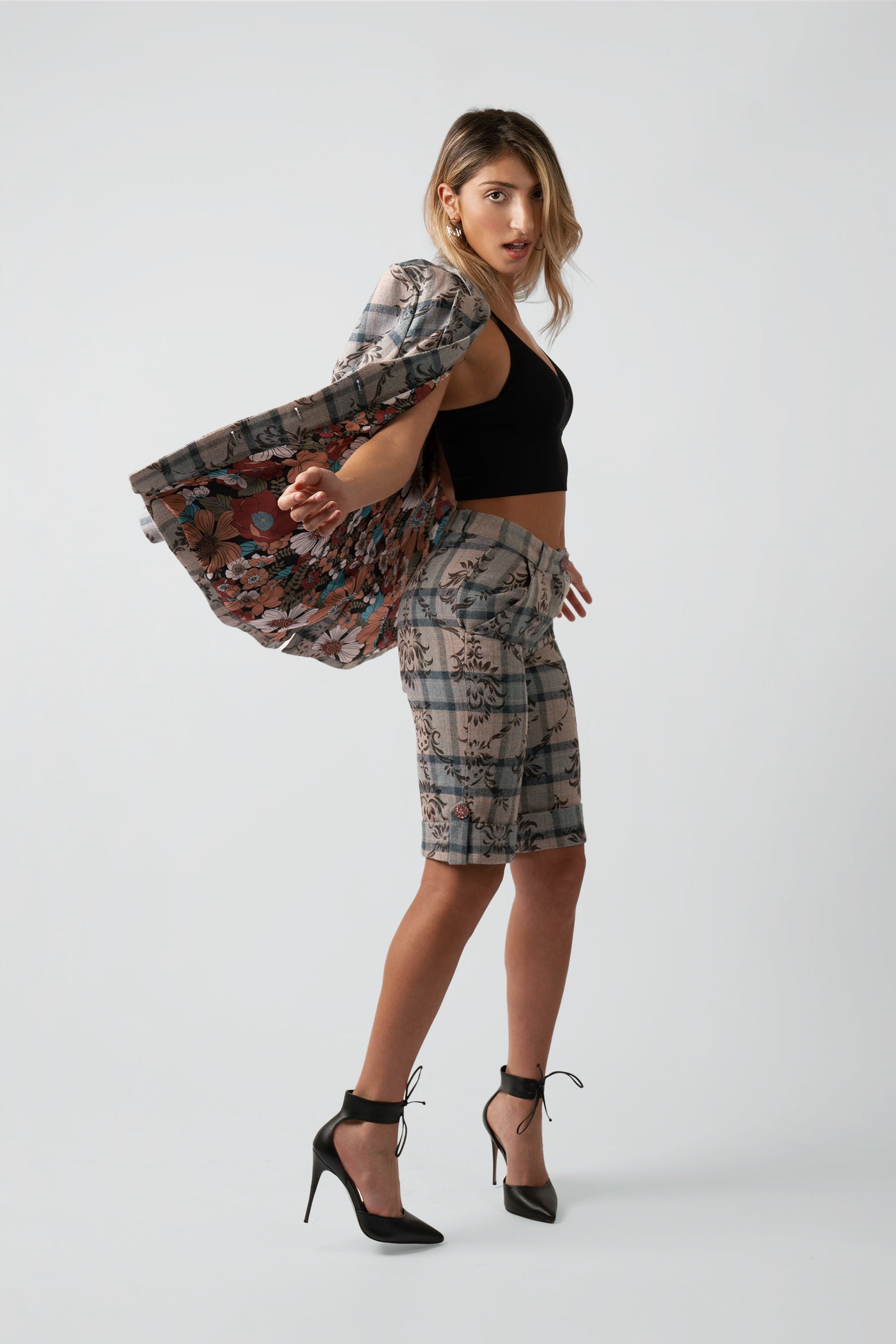 Woman wearing a floral and plaid patterned blazer over her shoulder and matching shorts posing against a white background