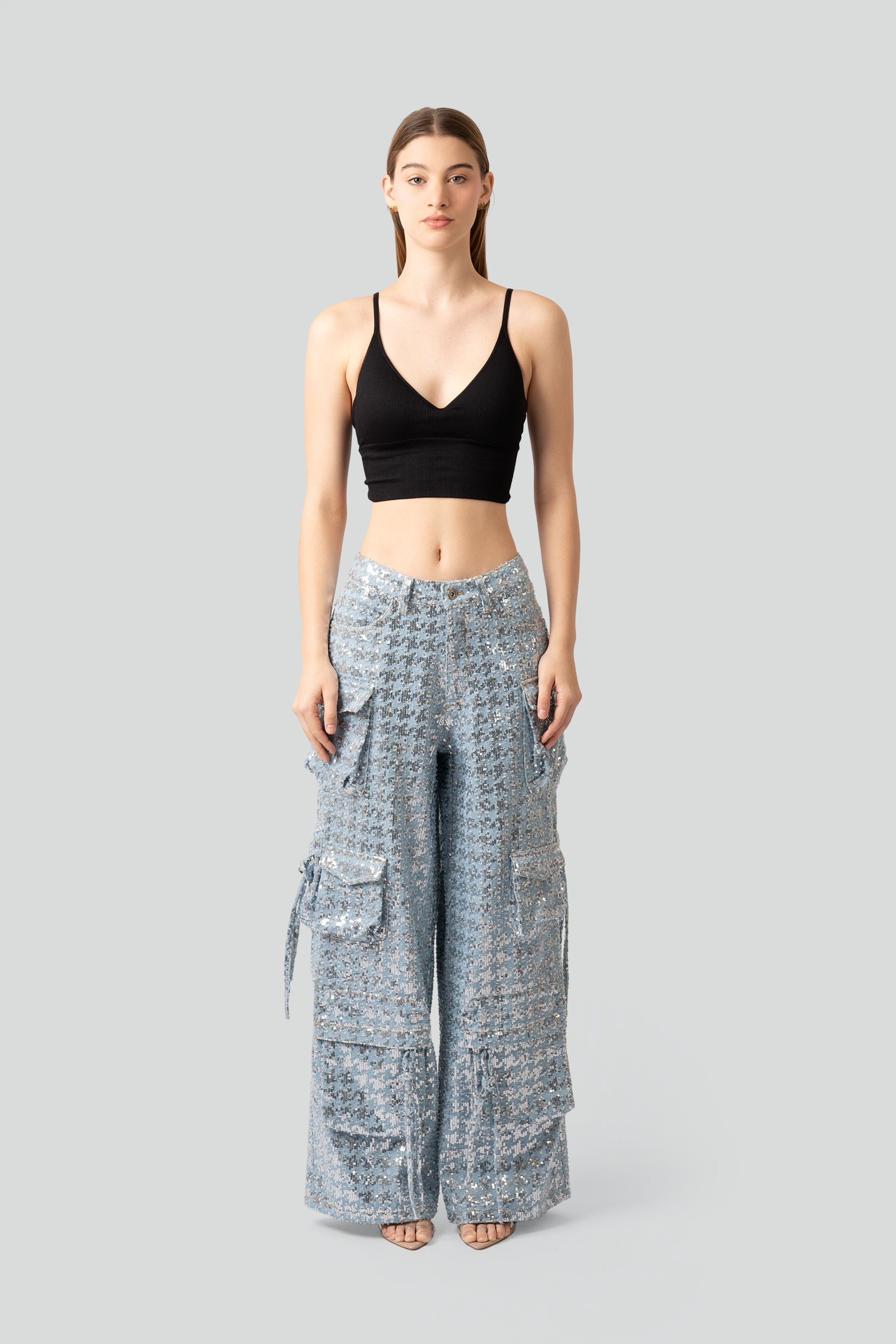 Woman wearing a black top and sequined cargo pants on a white background