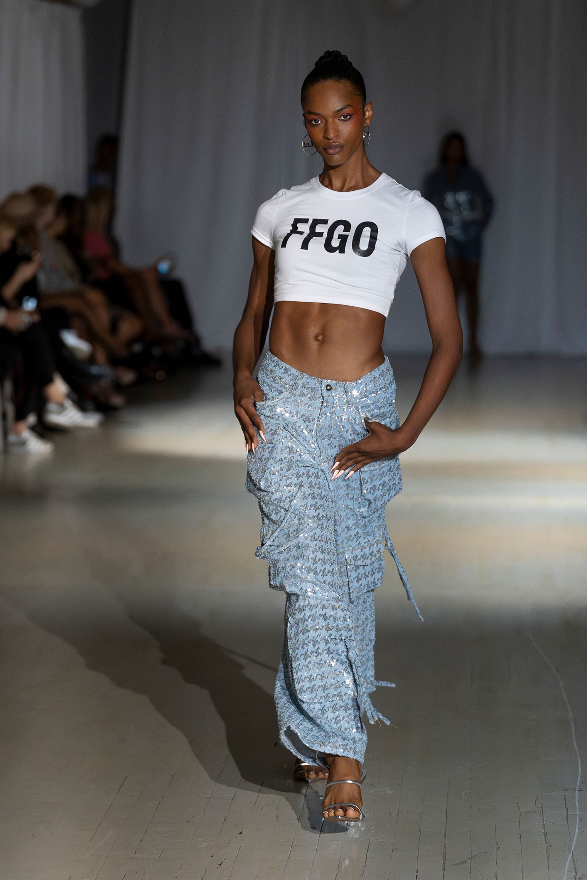 Model wearing a white crop top and sequined cargo pants walking the runway