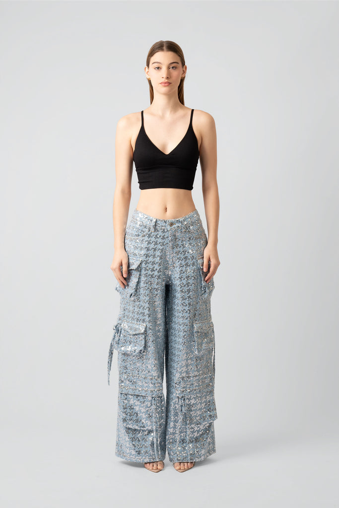 Woman wearing a black top and sequined cargo pants on a white background