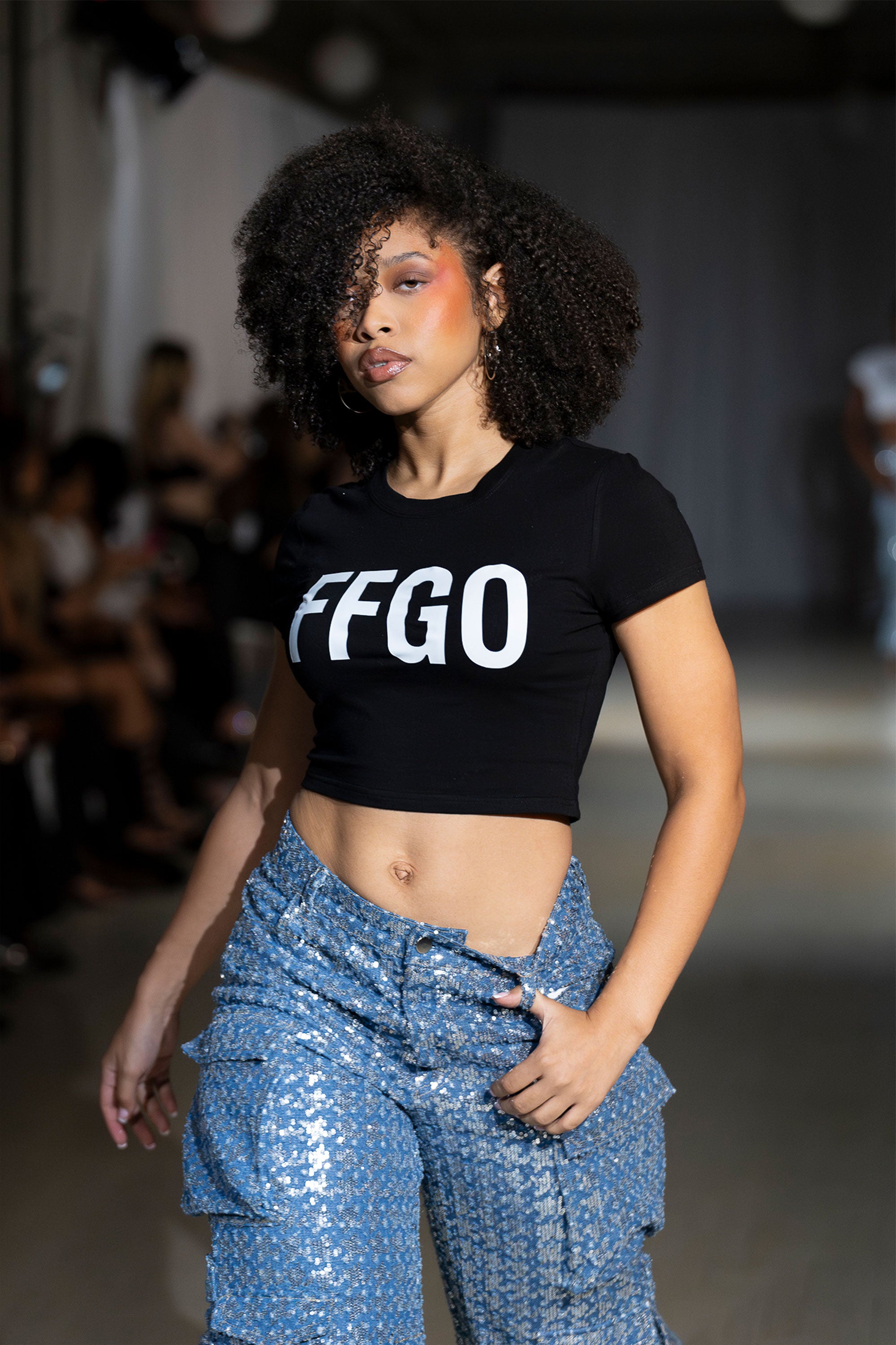 Model wearing a black crop top with the letters 'FFGO' walking down the runway