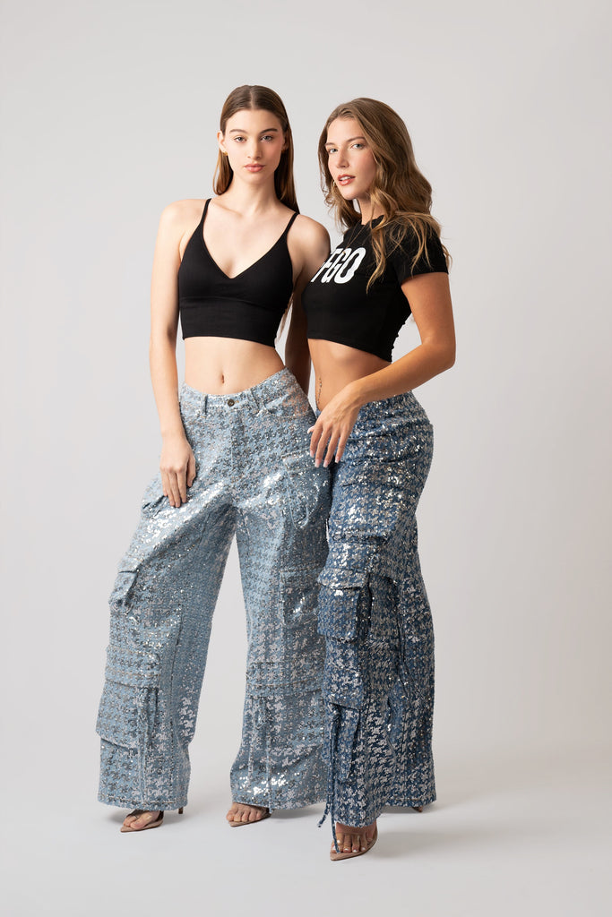 Two women wearing black crop tops and silver sequin pants on a plain background