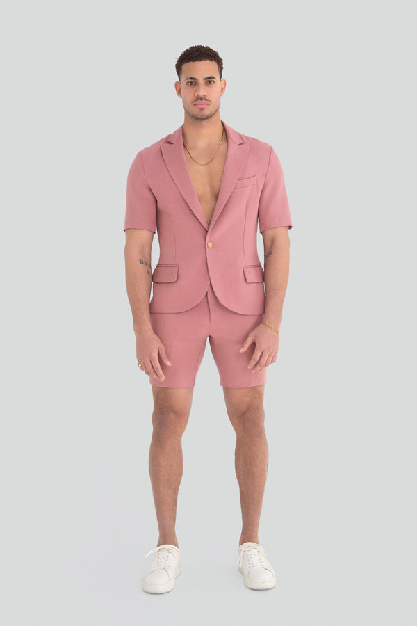 Model styling a luxury mens pastel pink two piece shorts set as a modern summer streetwear outfit with an architectural silhouette