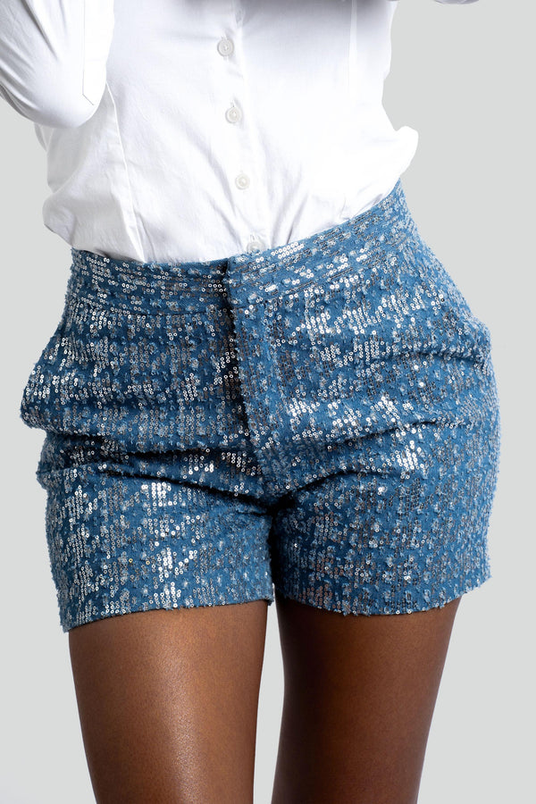 Close up view of blue cotton denim fabric highlighting the reflective sequin embroidery texture and precise pocket stitching