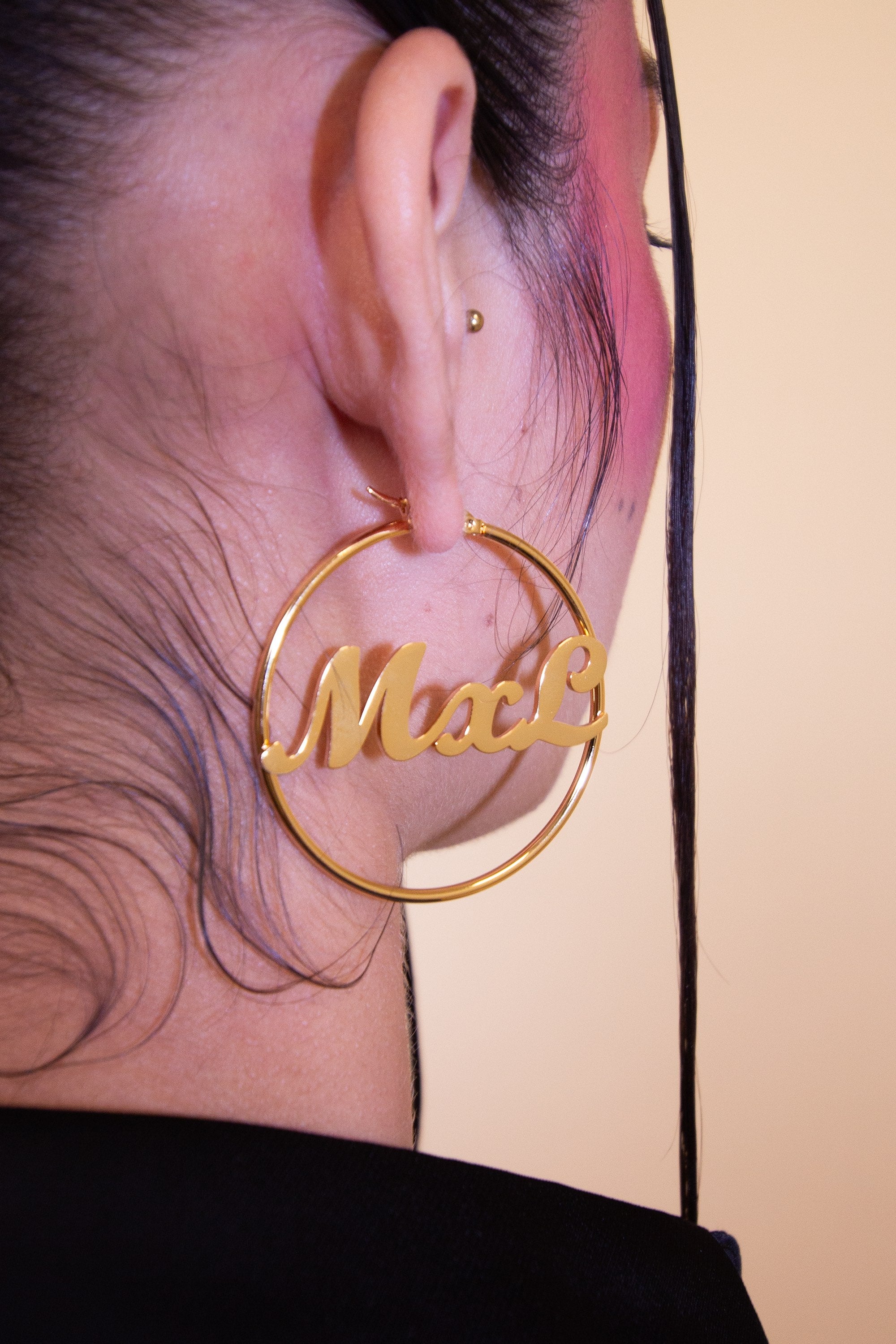 Woman wearing gold hoop earrings with 'MxL' engraving on a plain background