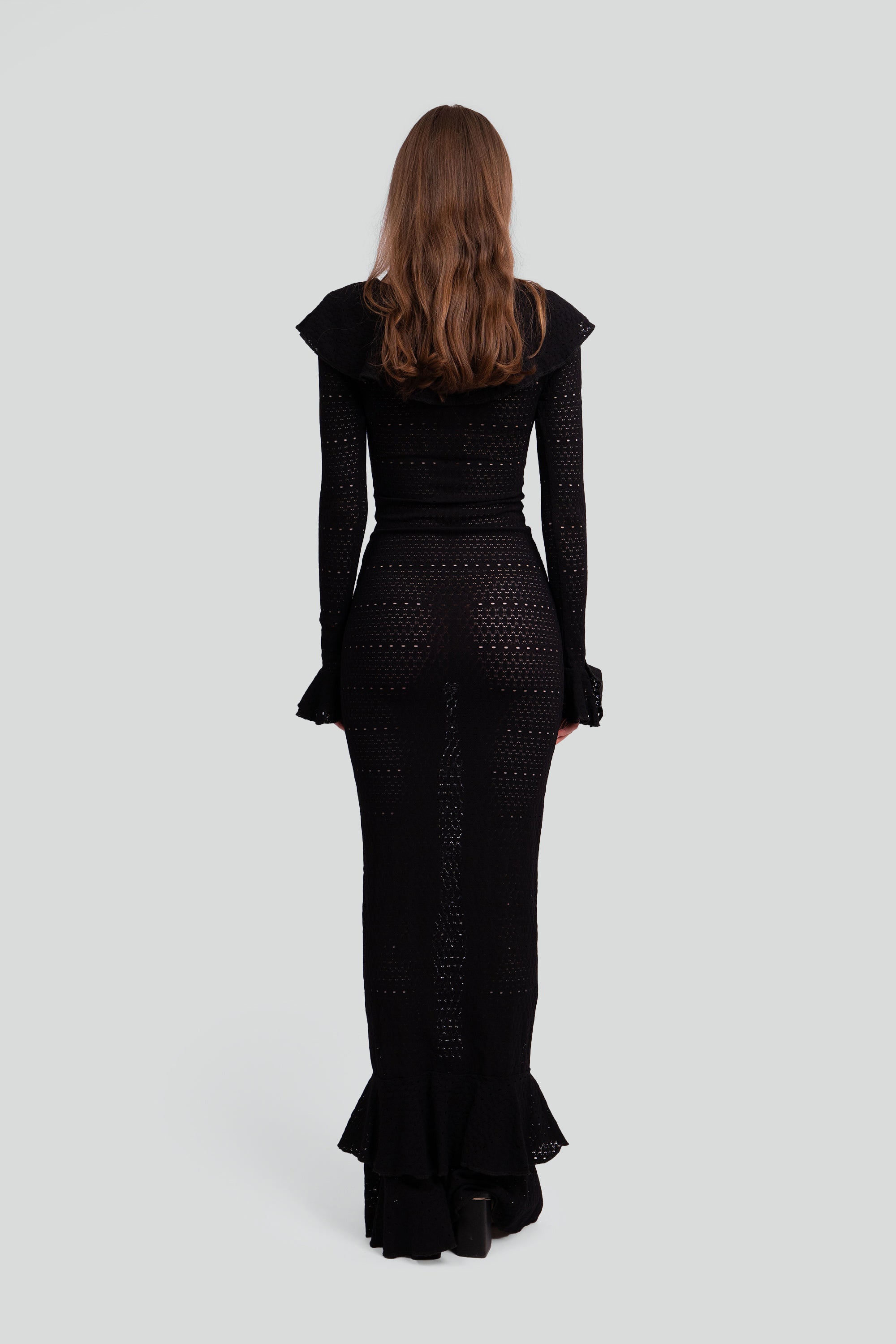 Back view of a woman wearing a black dress with ruffle detailing on a white background