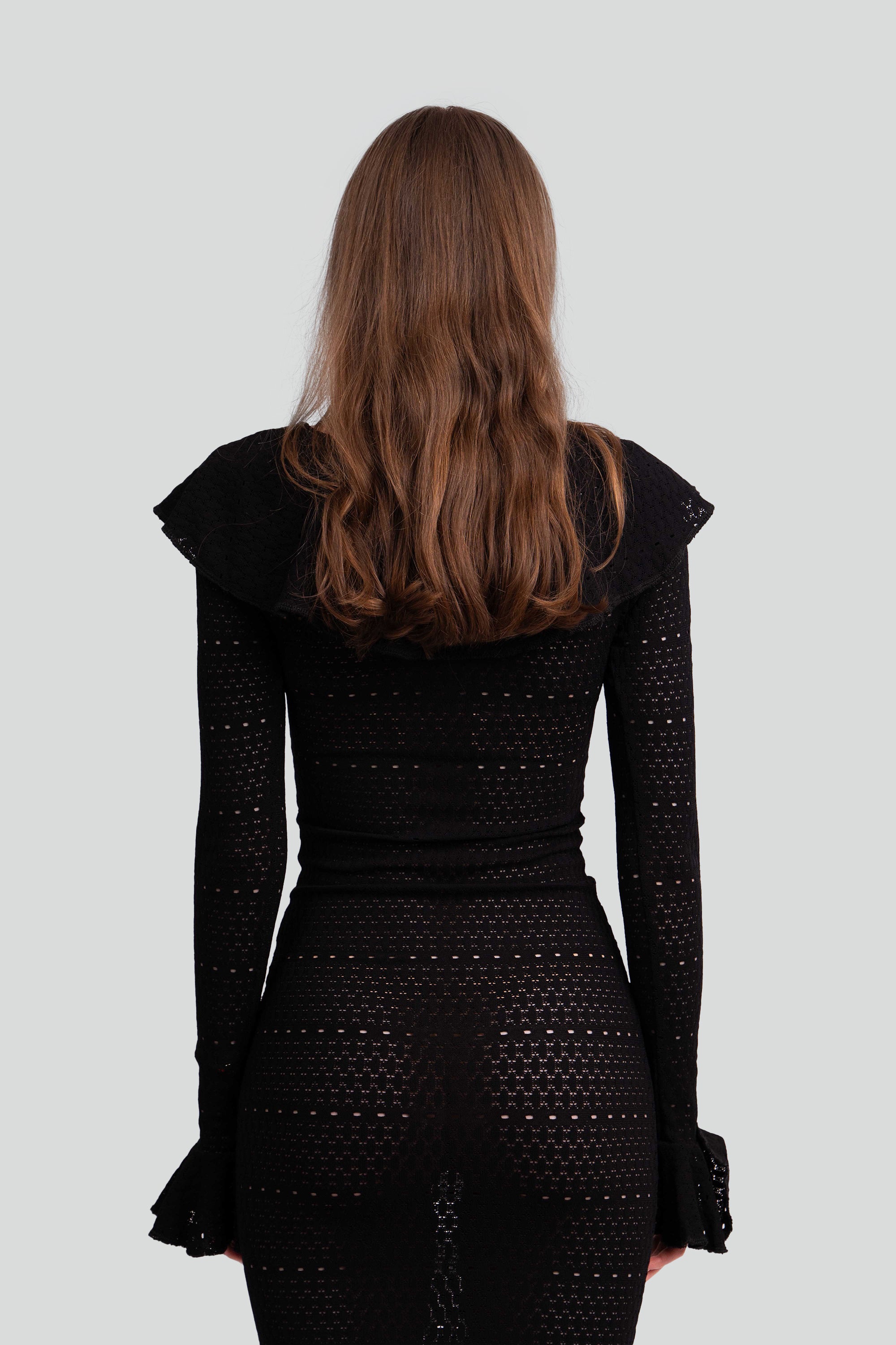 Close up back view of a woman wearing a black dress with intricate detailing on a white background