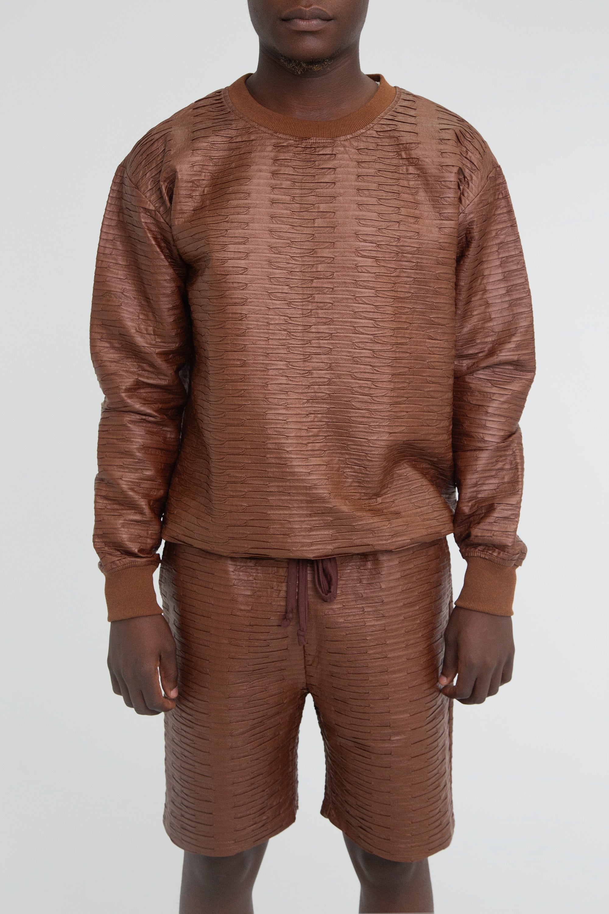 A brown textured leather outfit with long sleeves and shorts worn by a model on a plain background