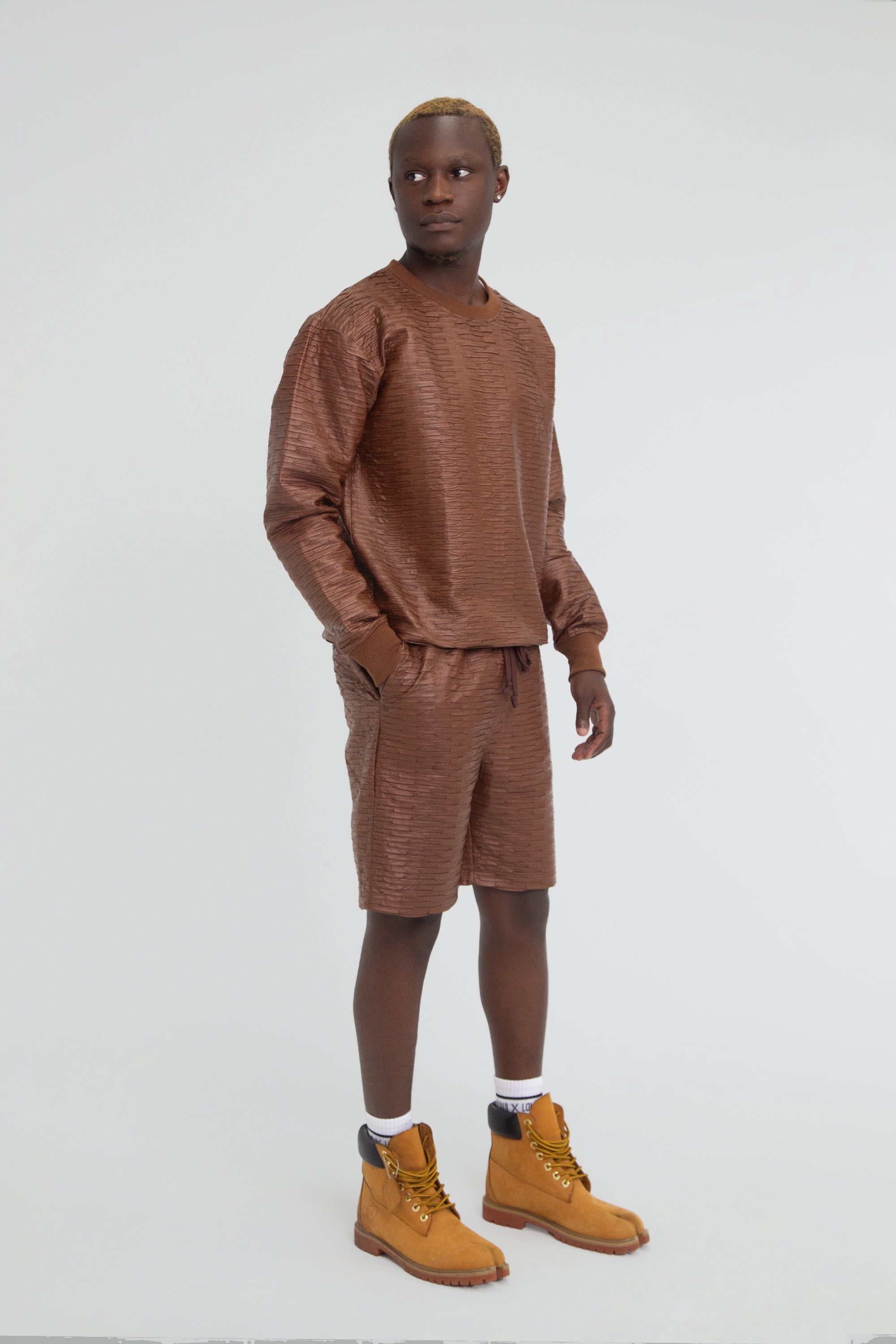 Man wearing a brown textured leather outfit with long sleeves and shorts on a plain background
