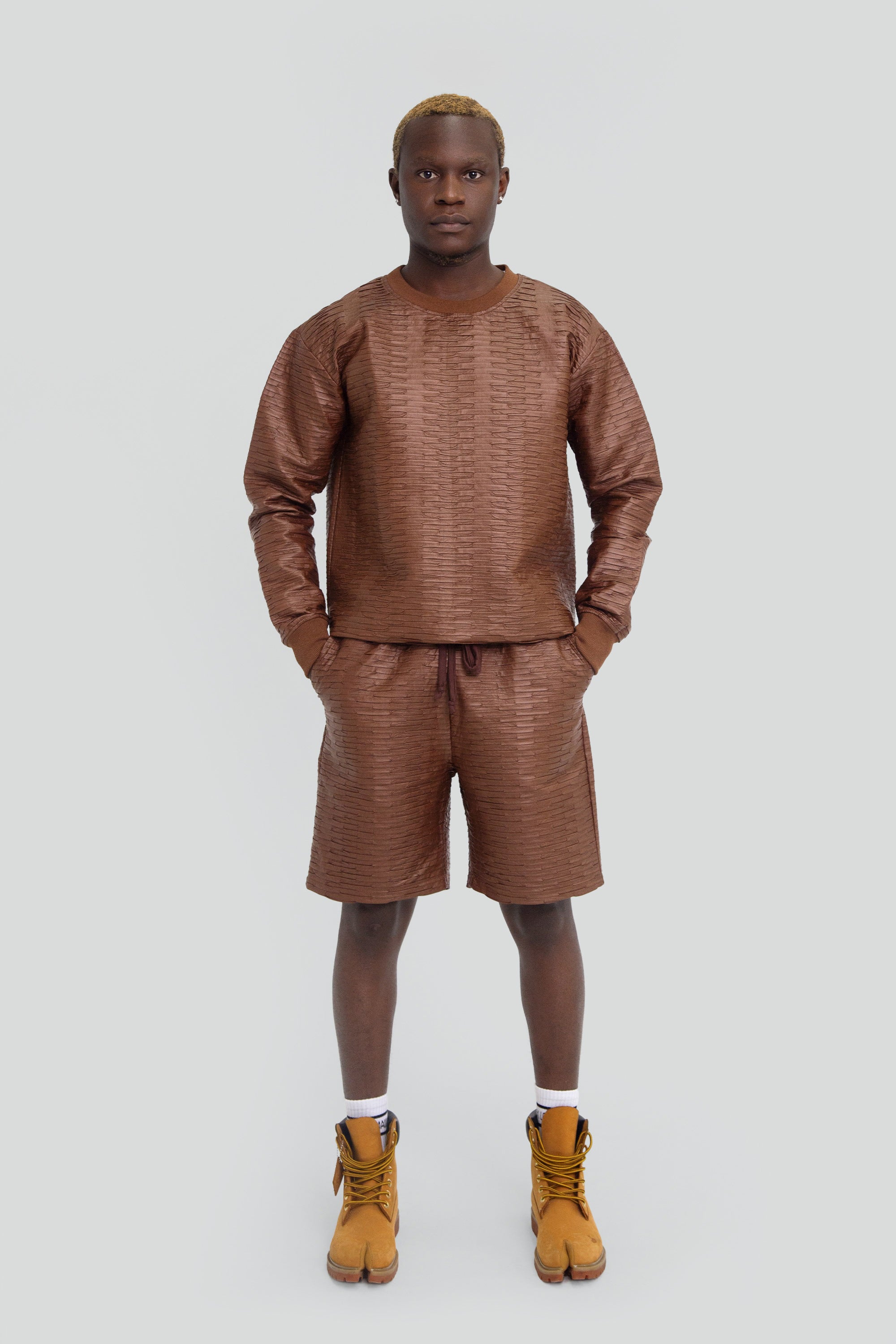 Man wearing a brown textured leather outfit with long sleeves and shorts on a plain background