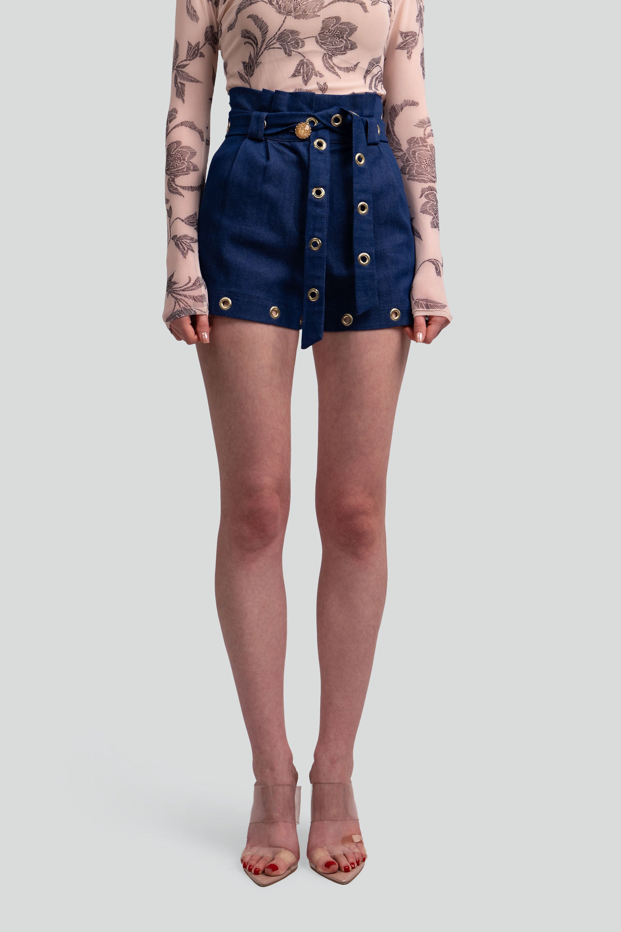 Person wearing navy denim shorts with gold grommets on a plain background