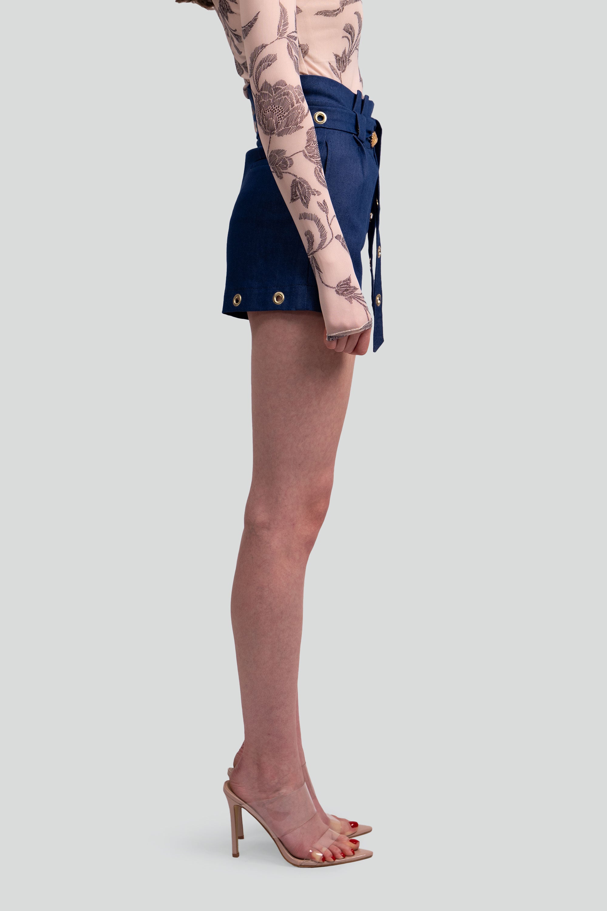 Person wearing navy denim shorts with gold grommets on a white background