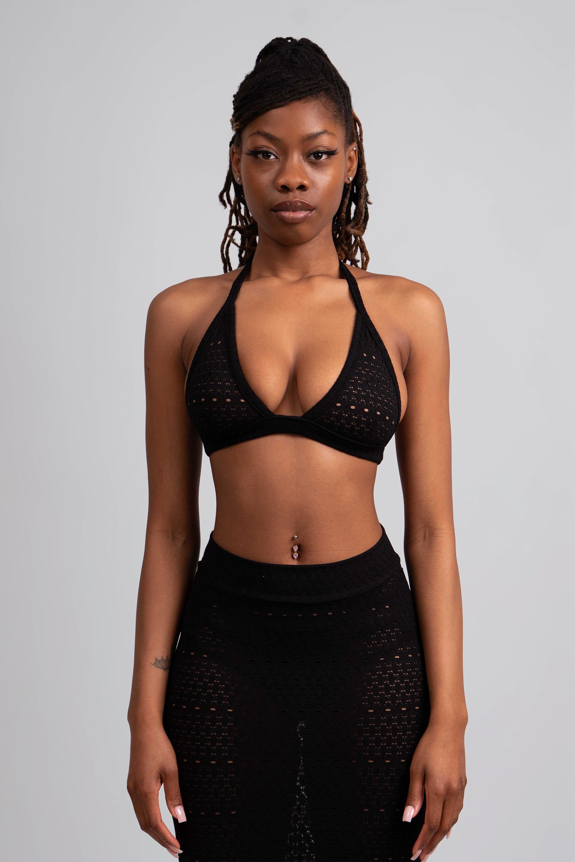 Close up of a woman wearing a black lace knit outfit with a halter top and ruffled skirt on a white background