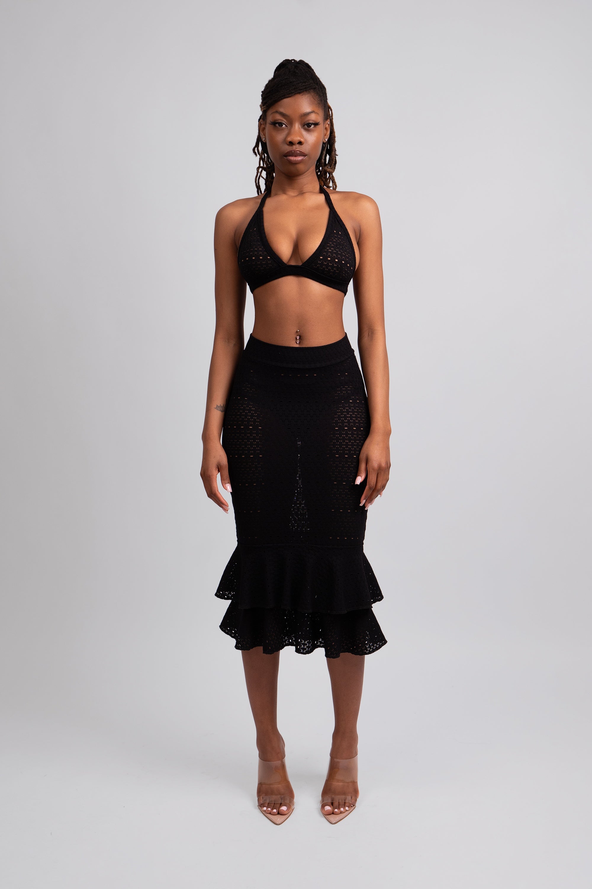 Woman wearing a black lace knit outfit with a halter top and ruffled skirt on a white background